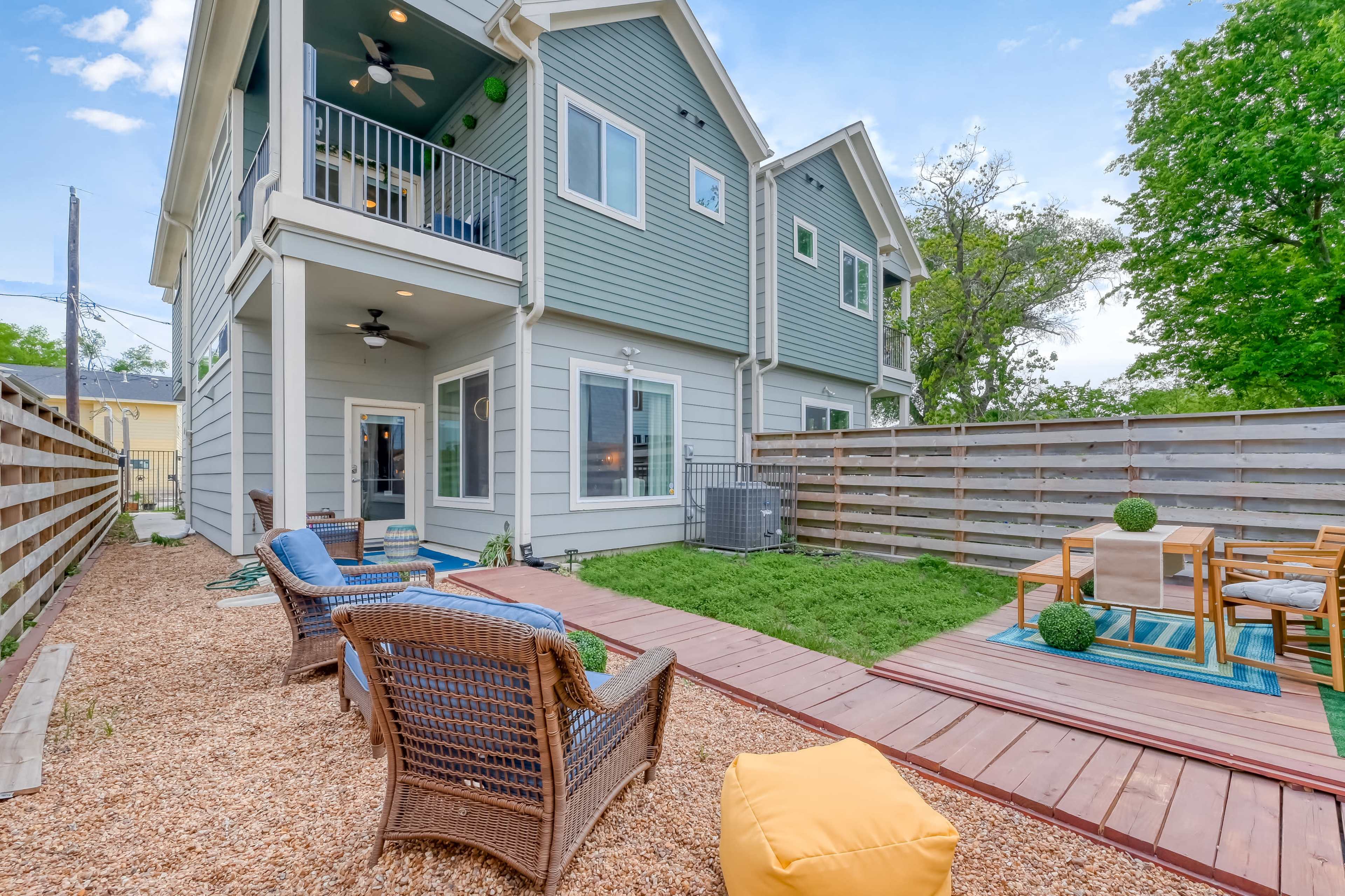 A backyard area featuring a deck with seating, a grassy space, and a modern two-story house.