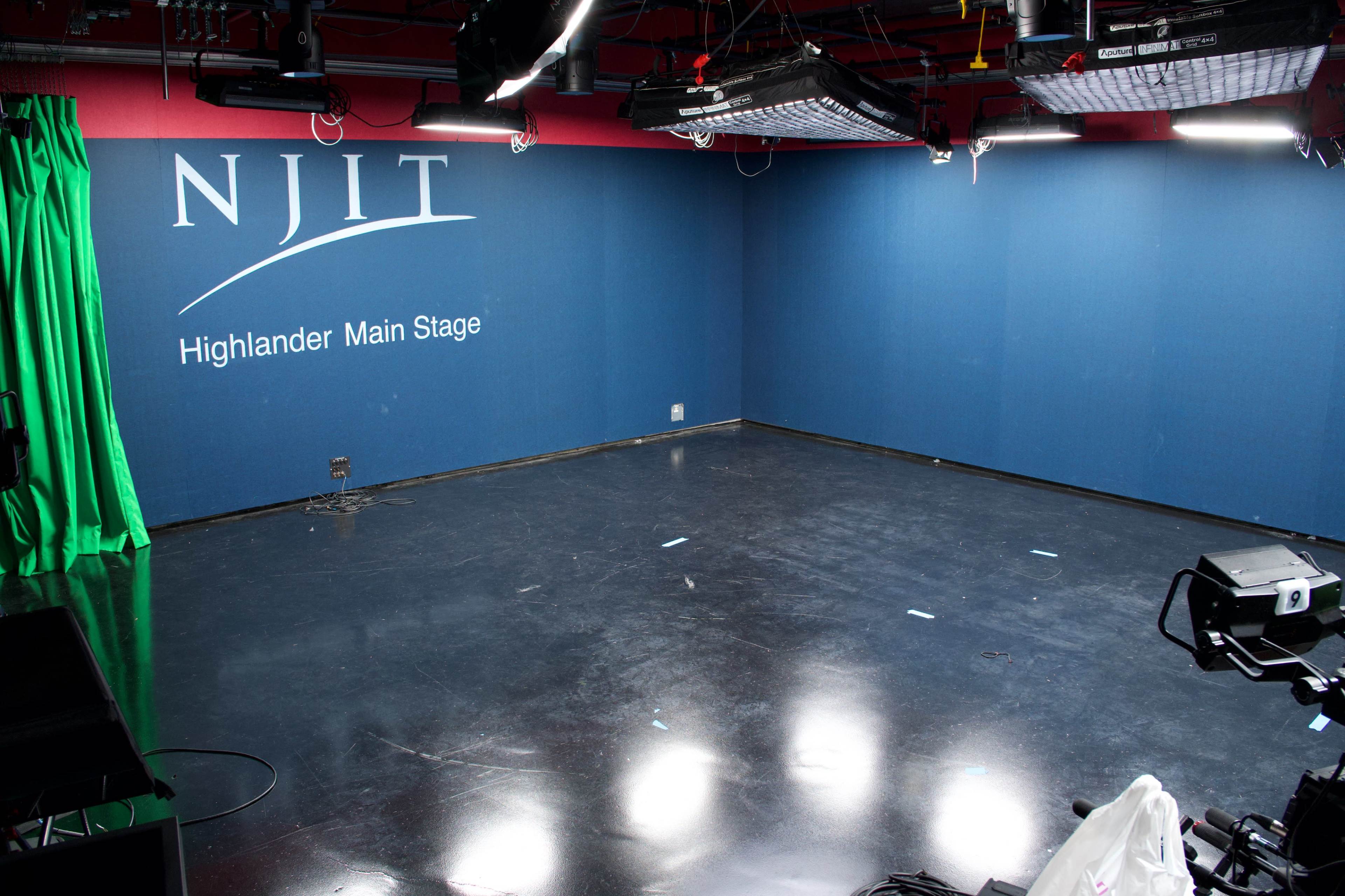 The image shows an empty television studio with a polished black floor, green curtains, and a blue backdrop featuring the text "NJIT Highlander Main Stage."