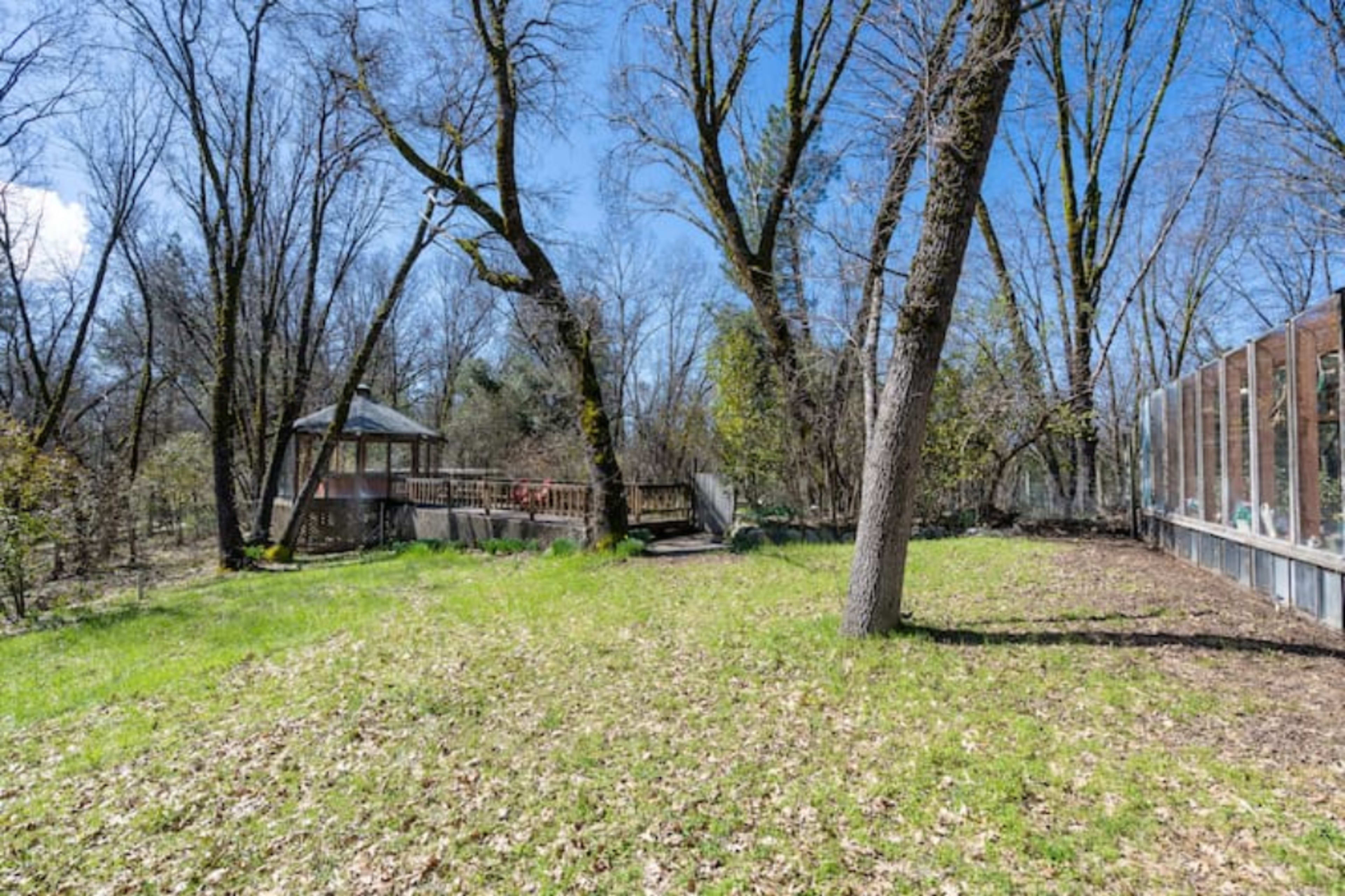 A grassy area with scattered trees and a gazebo is visible beside a wooden deck and a glass-enclosed structure.