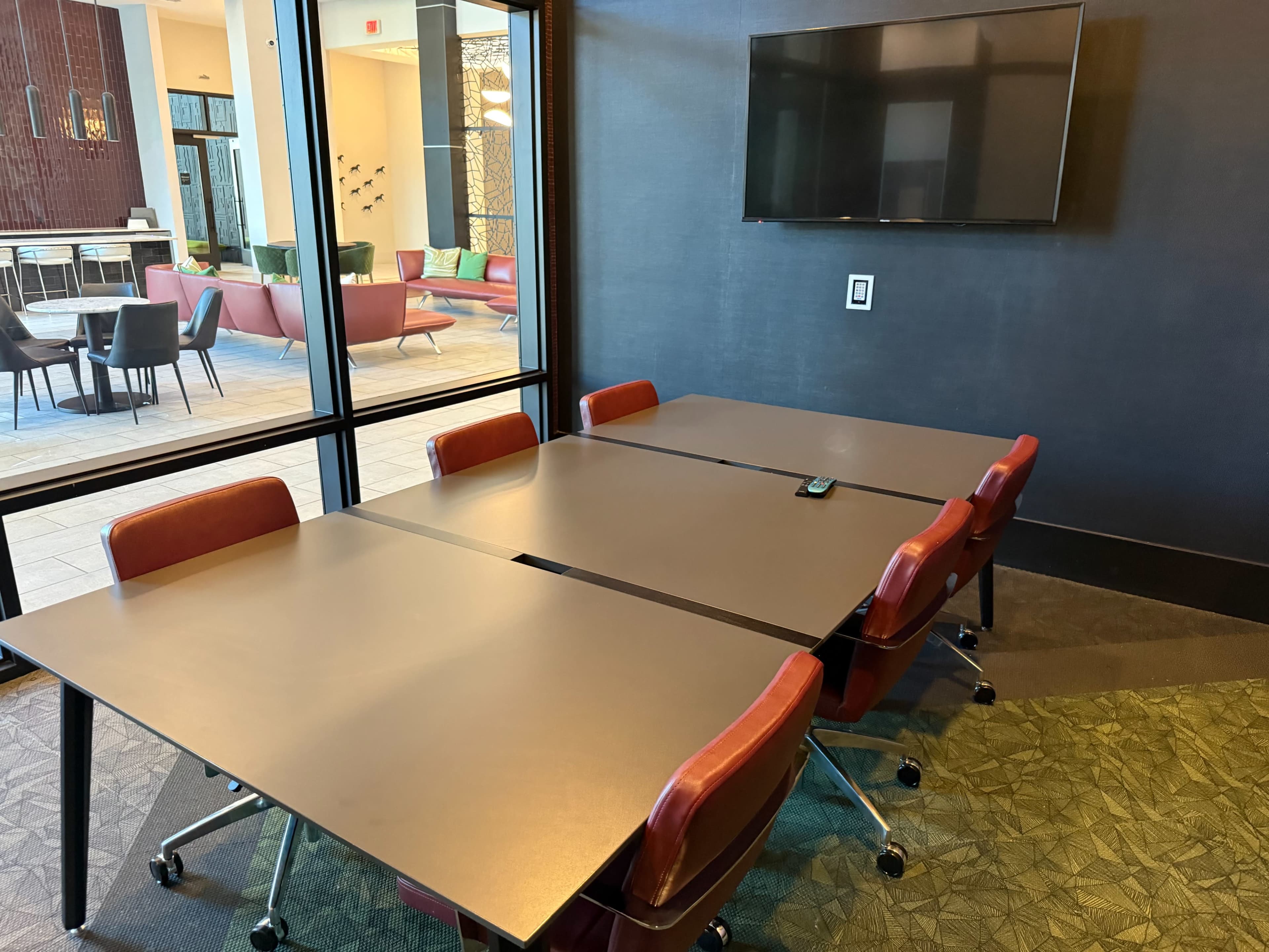 The image shows a modern conference room with a large table and several red chairs, along with a wall-mounted television.