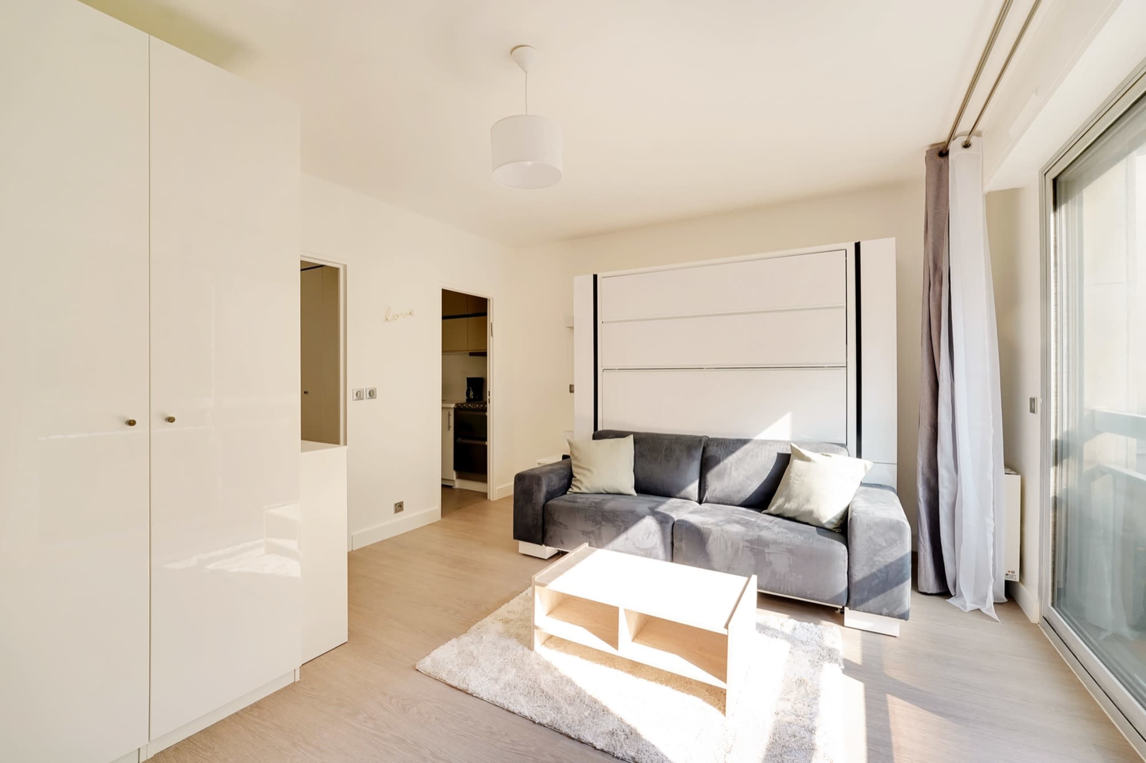 The image shows a modern living room with a gray sofa, a light wooden coffee table, and built-in storage cabinets against one wall.