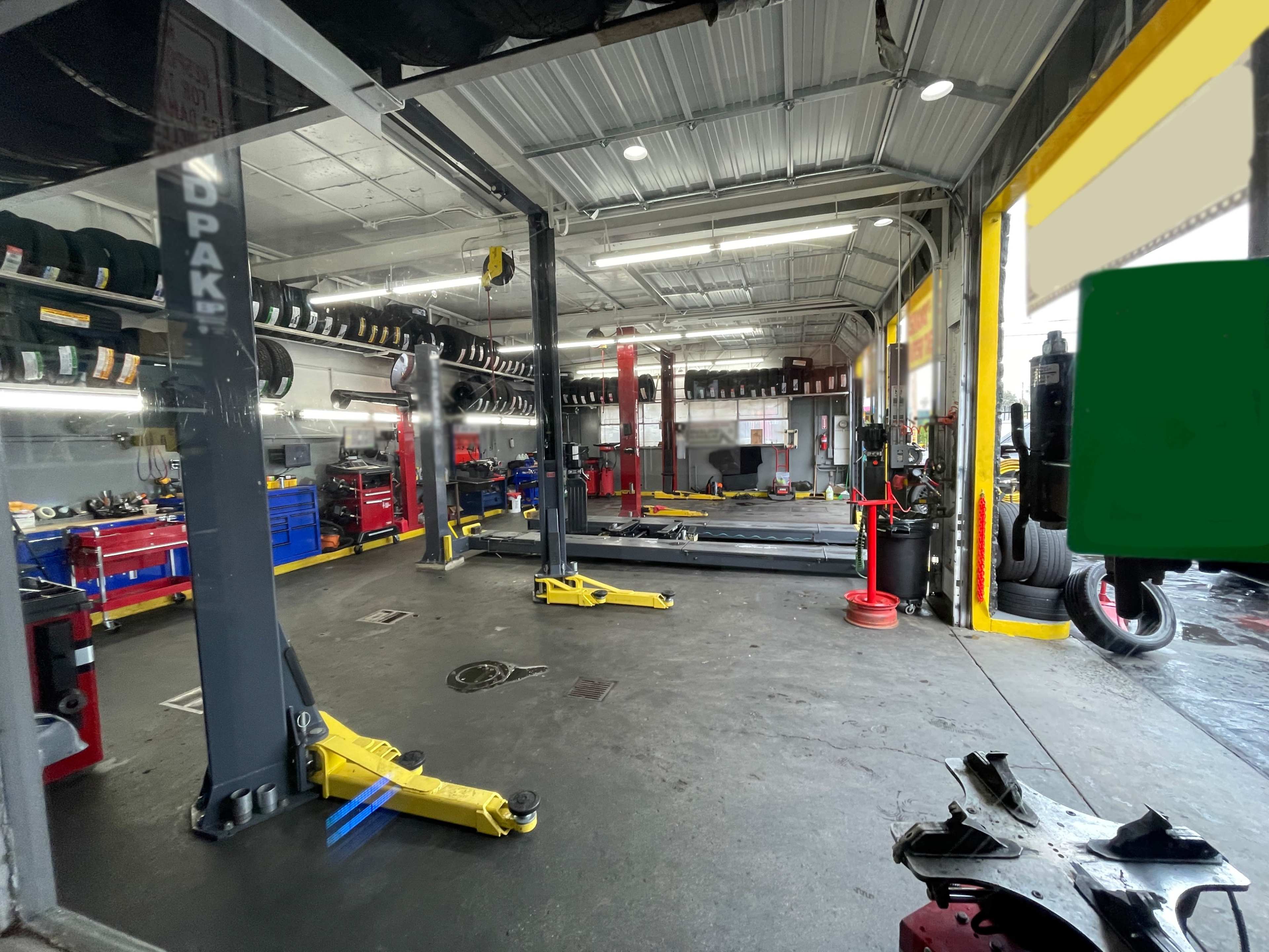 The image shows an auto repair shop with multiple vehicle lifts, tool storage areas, and tires mounted on racks in the background.