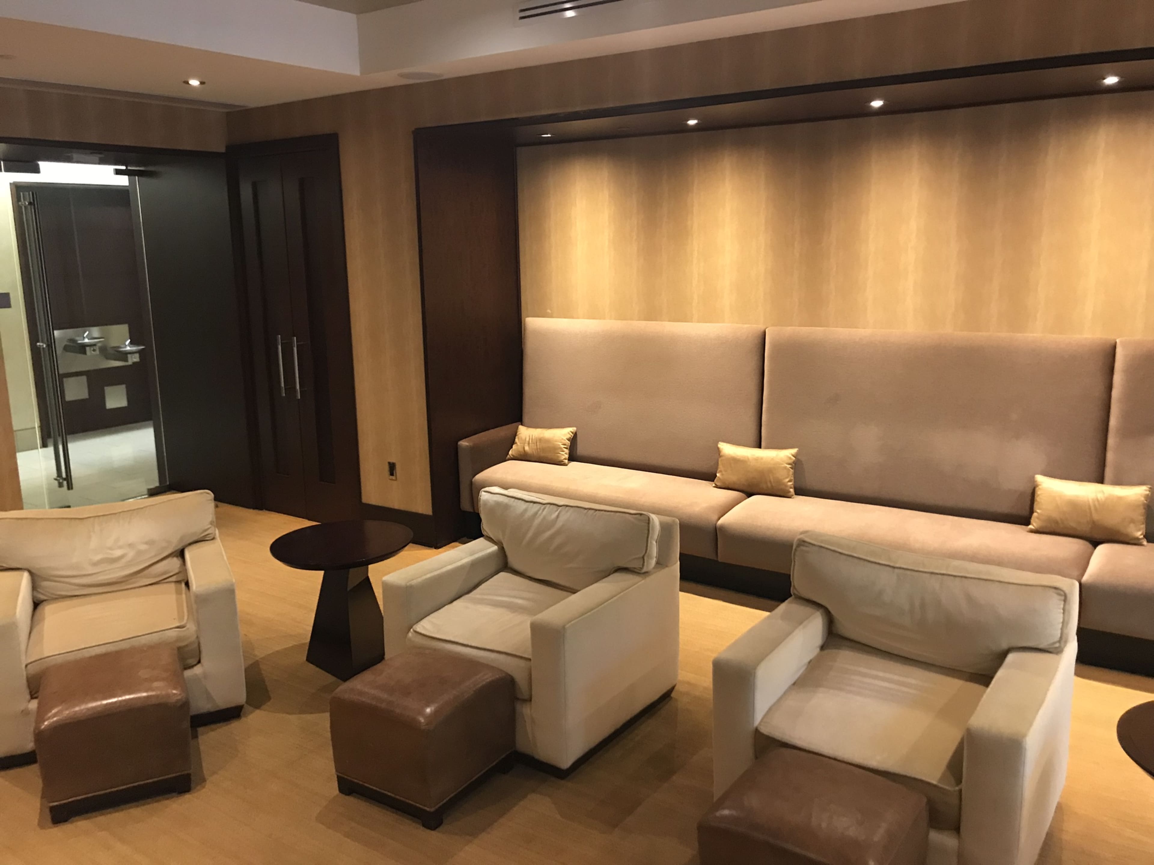 A modern lounge area with a beige sofa, two armchairs, and a small table, set against a softly lit wall.