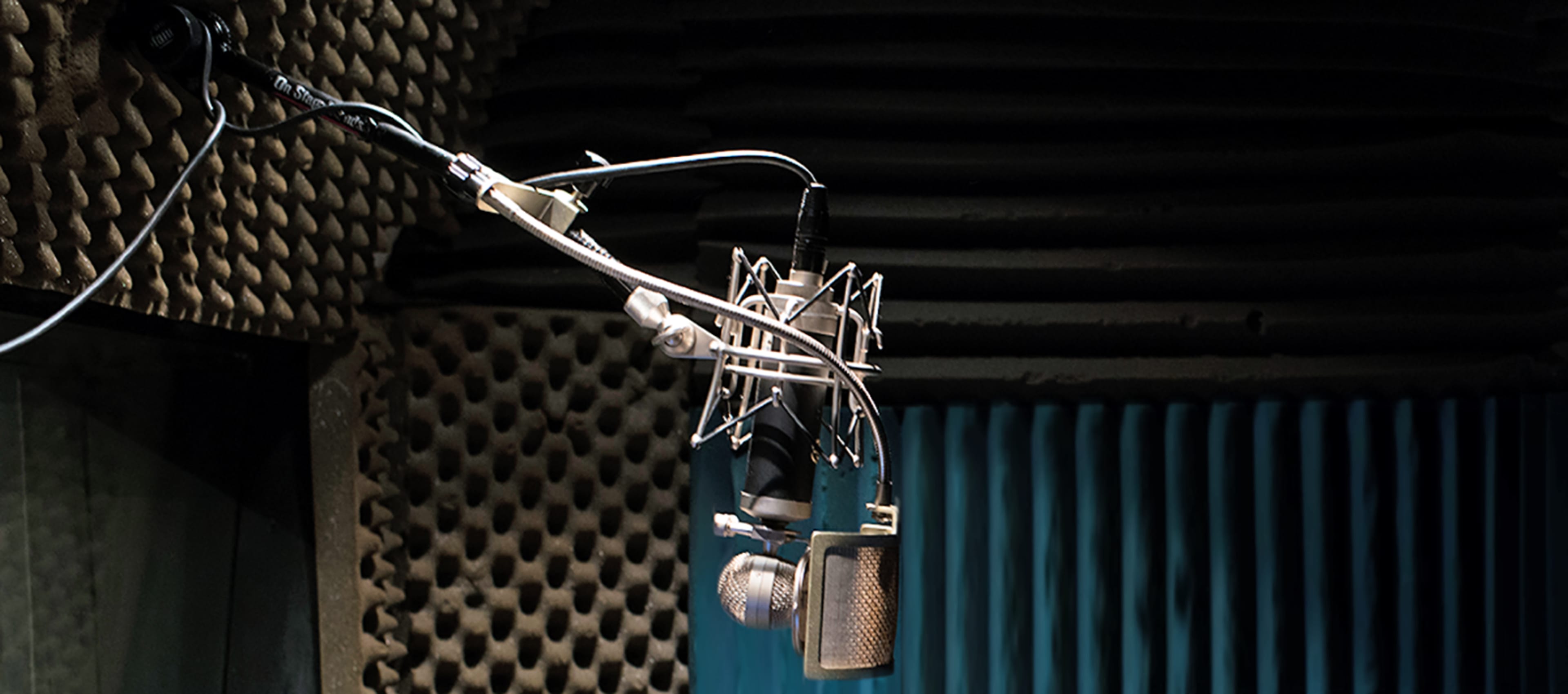 A microphone hangs from a stand in a soundproof recording studio.