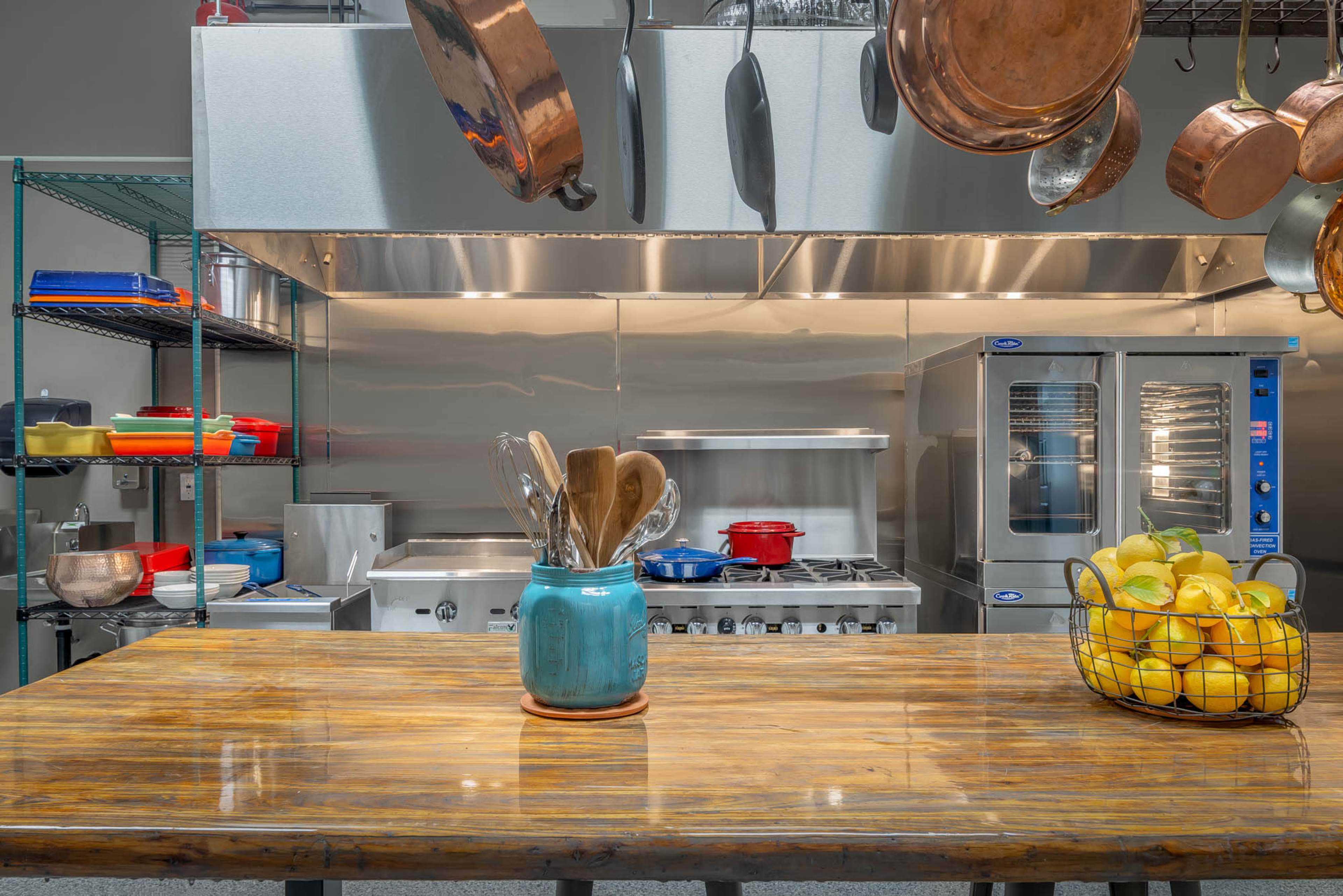 A spacious kitchen features stainless steel appliances, a wooden table with utensils, and a basket of lemons.
