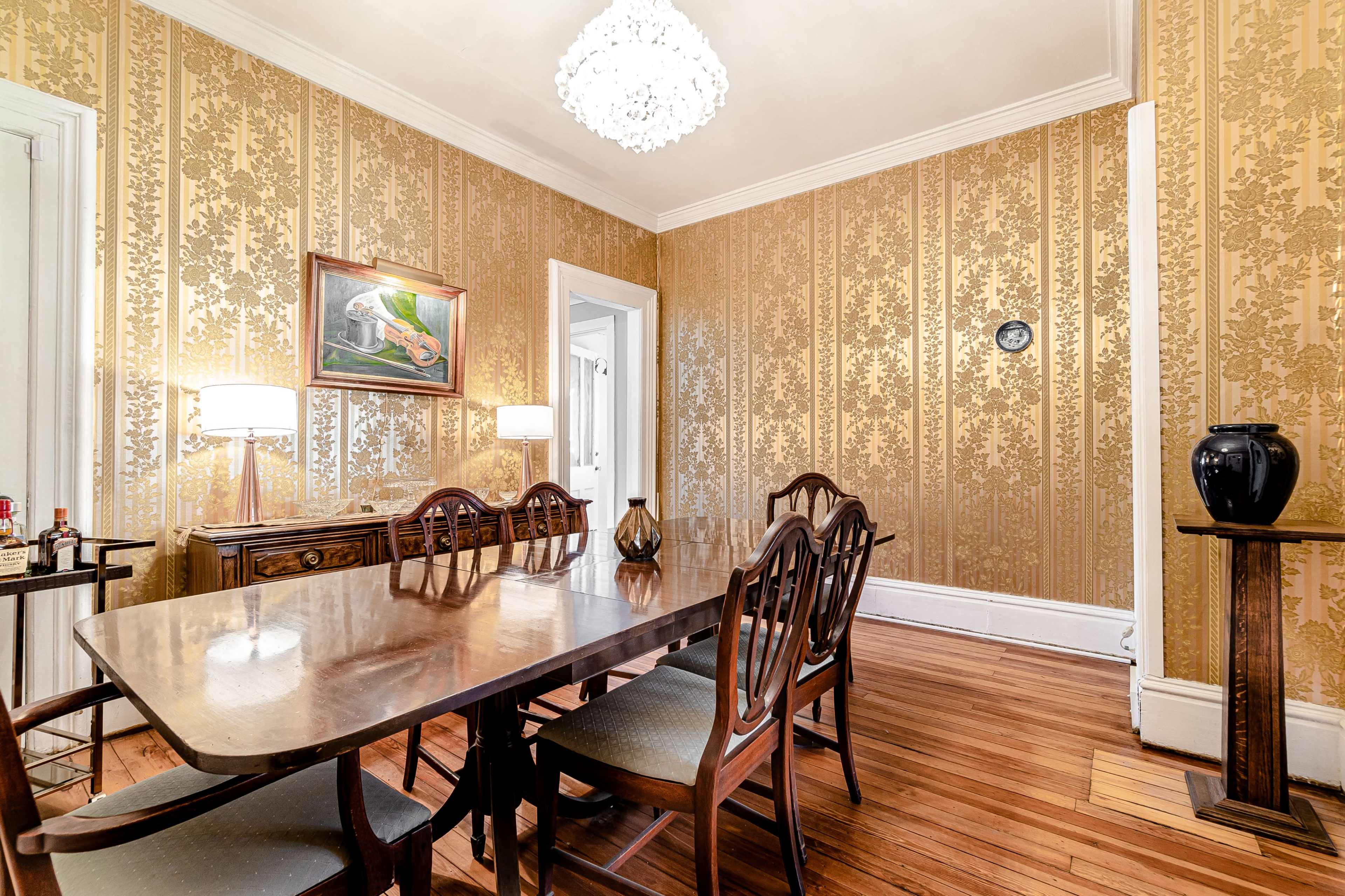 A dining room featuring a wooden table with chairs, ornate wallpaper, and a chandelier.