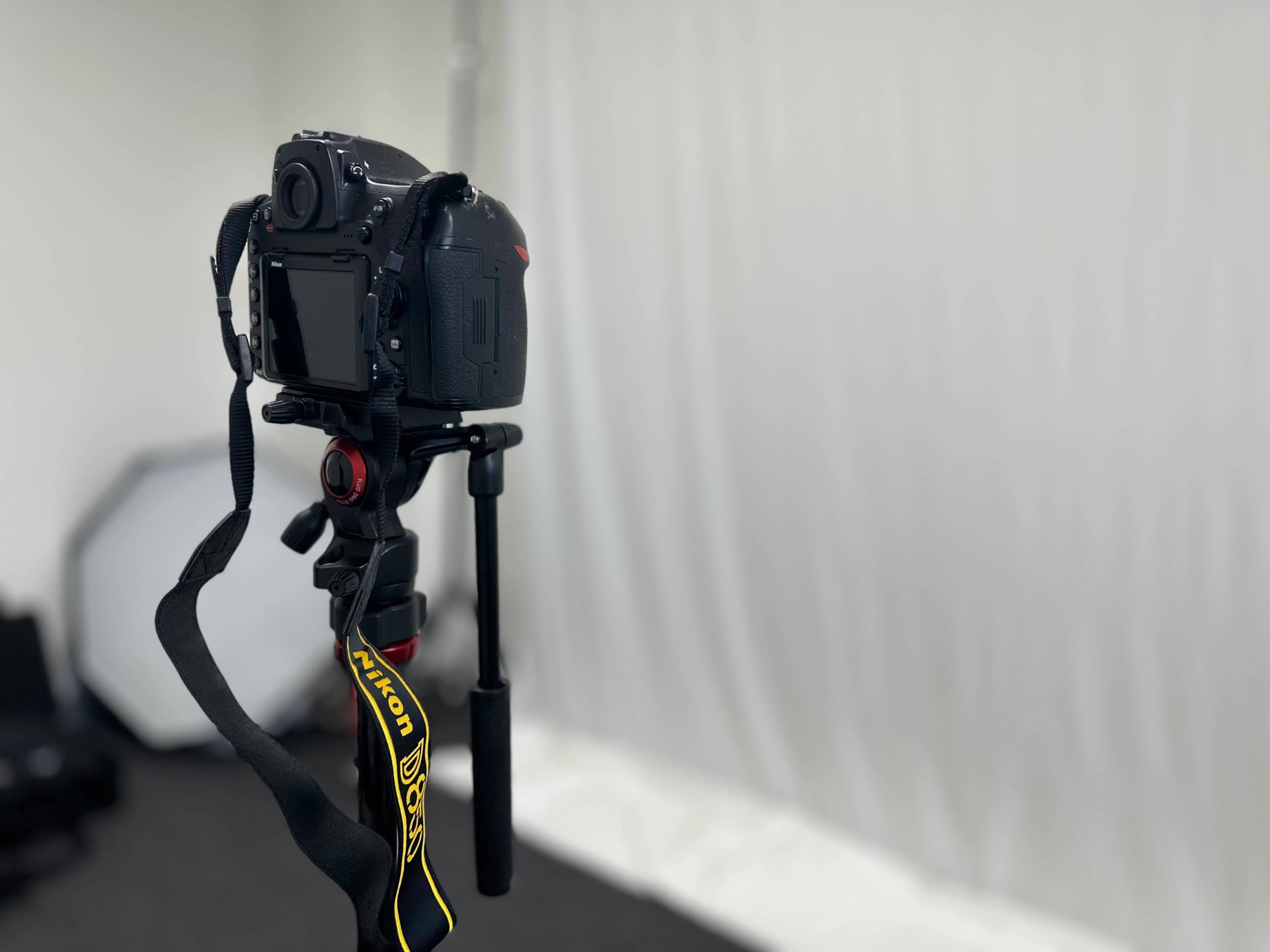 A Nikon camera is mounted on a tripod, facing a plain white backdrop in a studio setting.