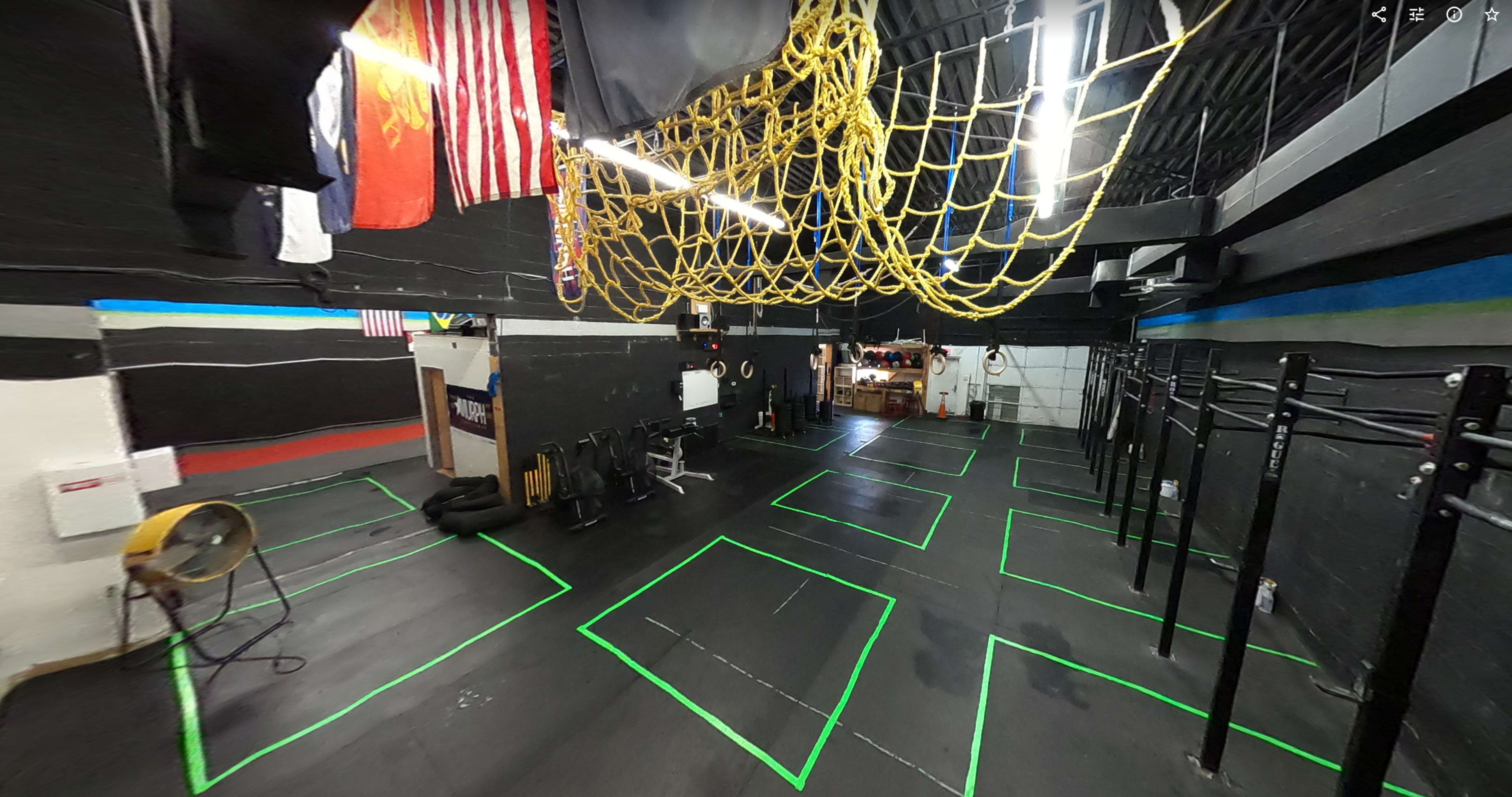 An indoor gym space with marked workout areas, gym equipment, and a colorful net hanging from the ceiling.
