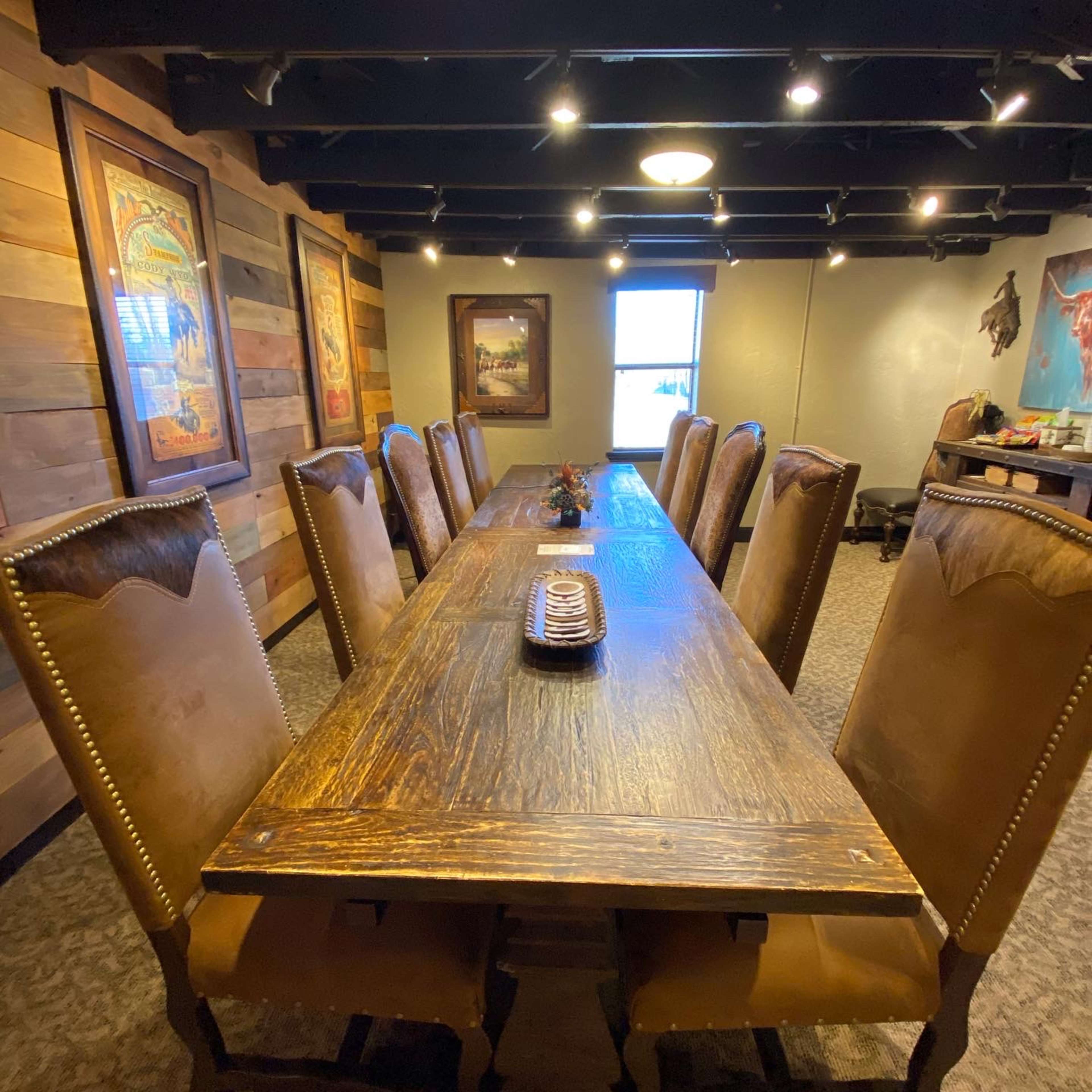 A long wooden dining table with upholstered chairs is set in a room featuring wooden walls and decorative artwork.