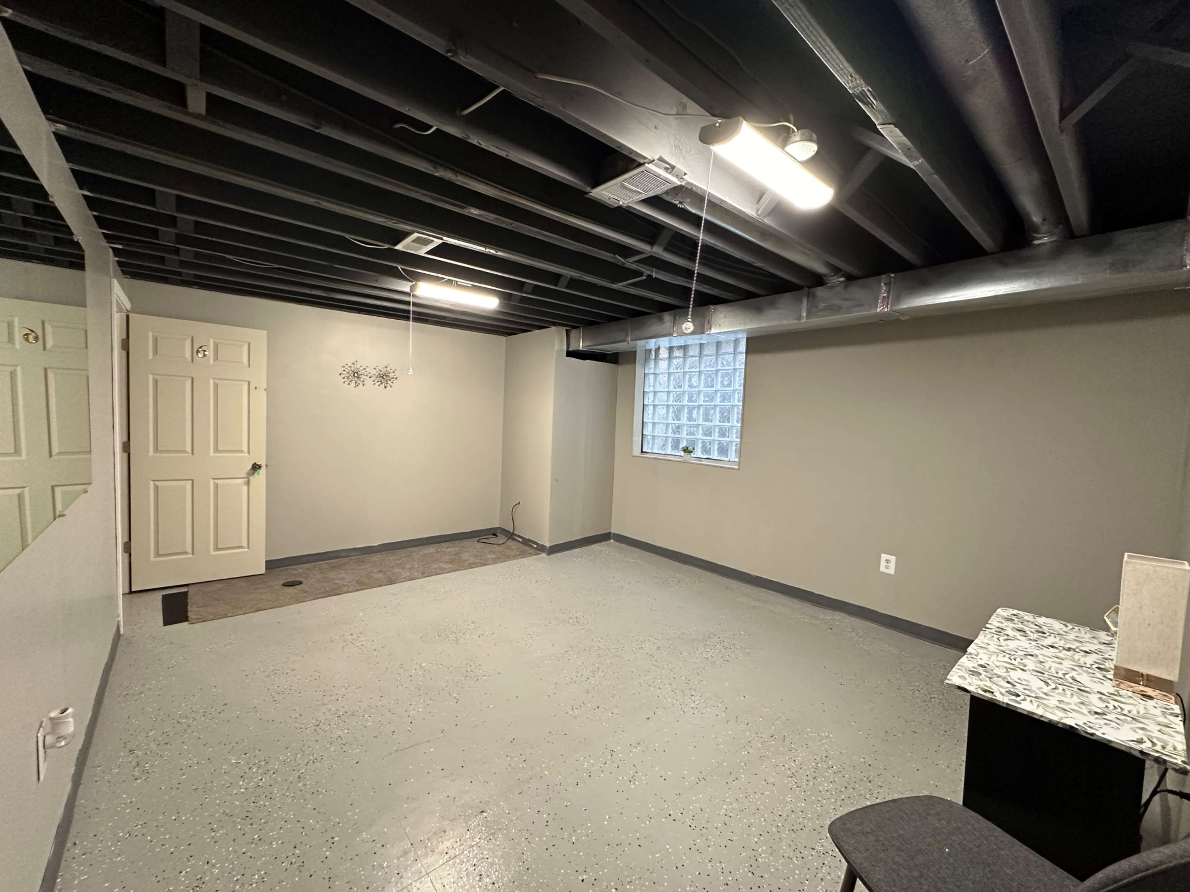A finished basement with gray walls, a concrete floor, a window, and a small desk in one corner.