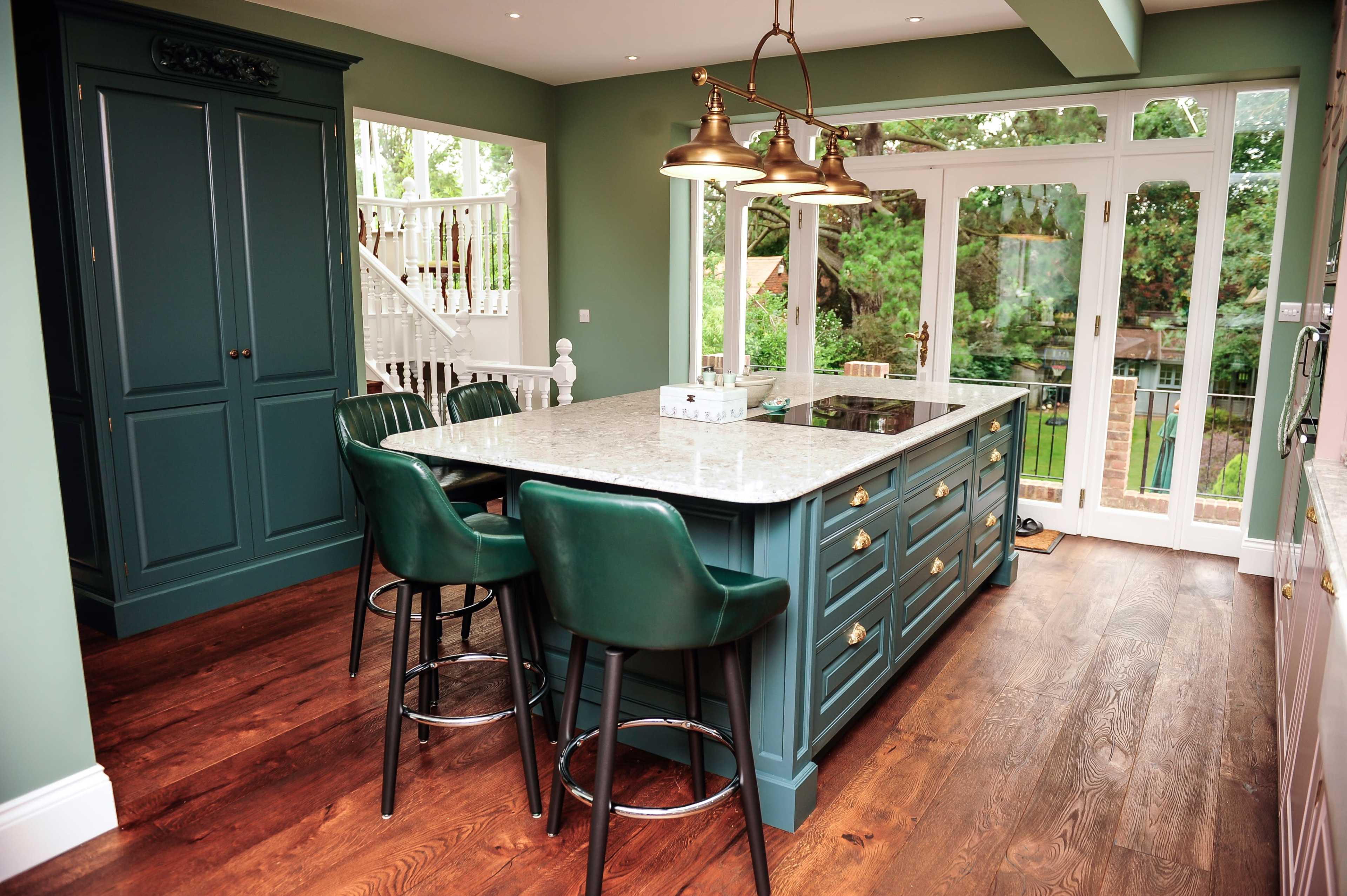 A modern kitchen with a green island, granite countertop, and four dark green bar stools.