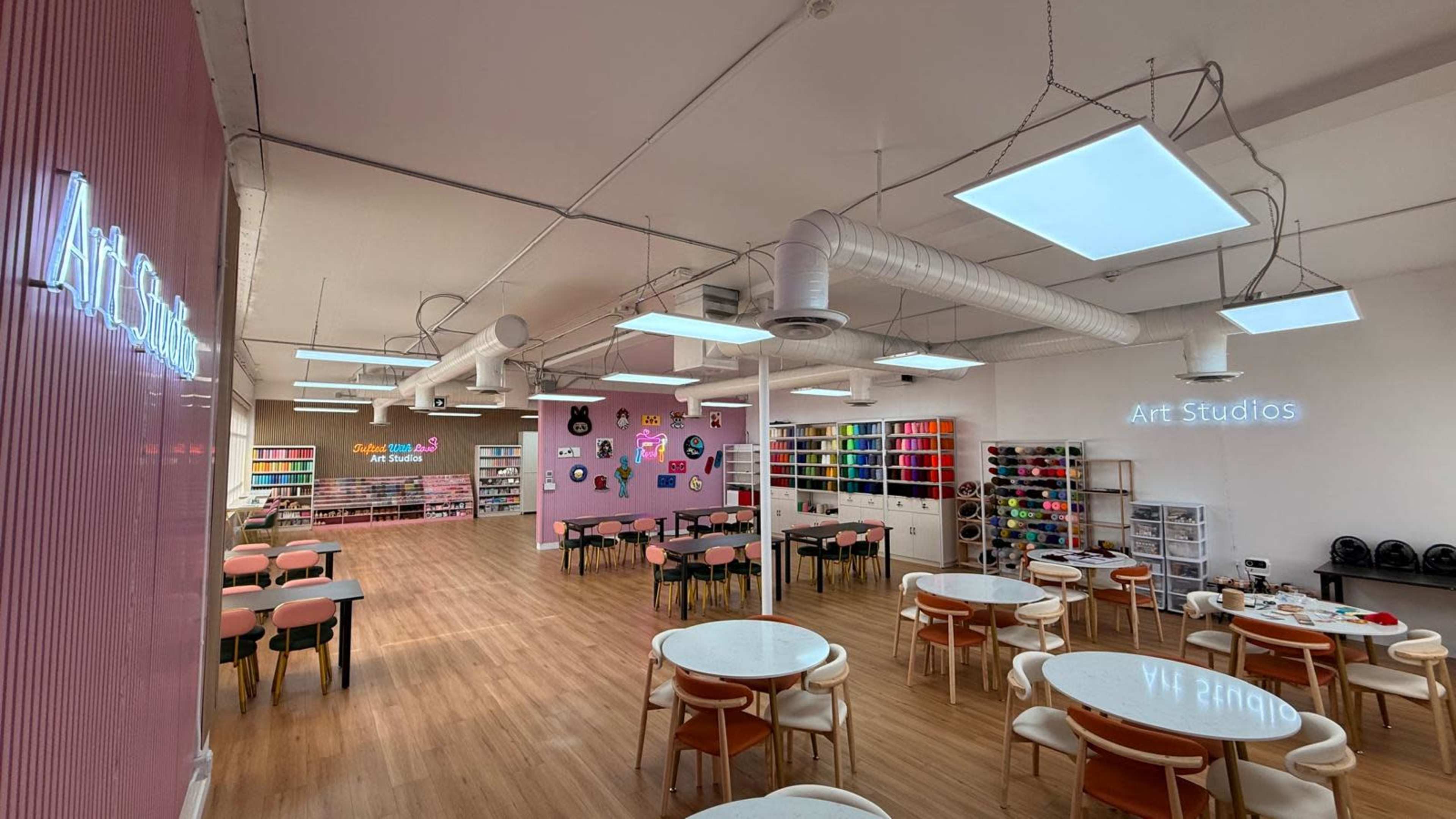 The image shows a spacious, modern art studio with various tables, colorful storage shelves, and vibrant decorations on the walls.