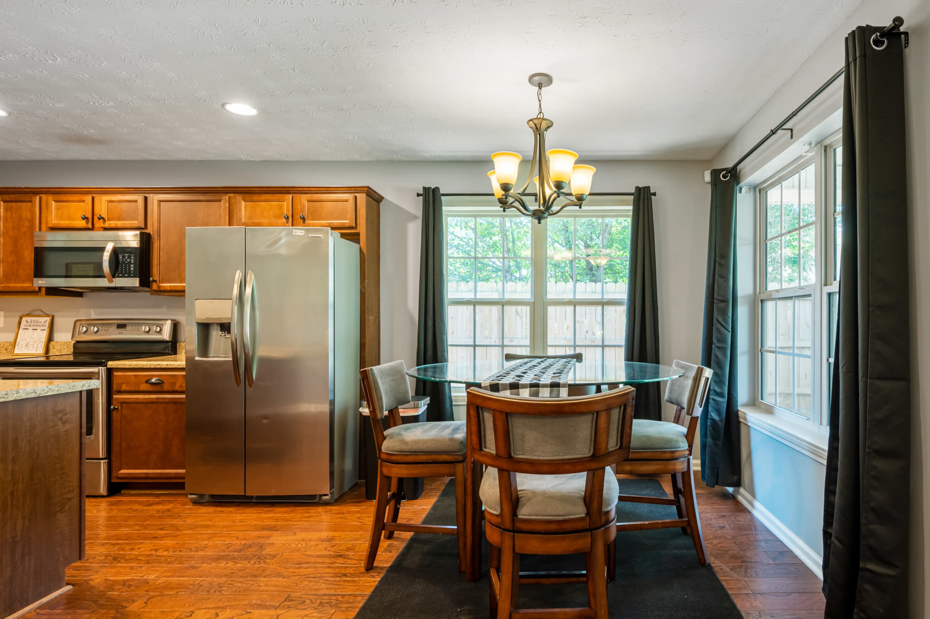 A kitchen features wooden cabinets, a stainless steel refrigerator, and a glass-topped dining table with four chairs.