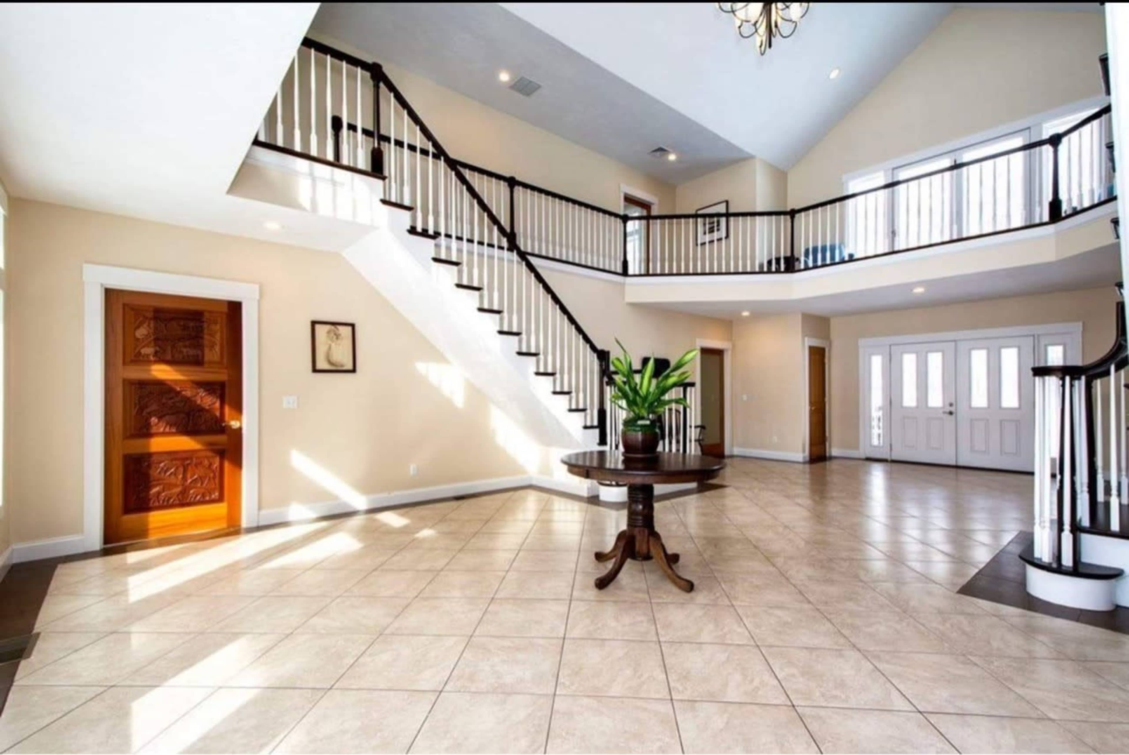 A spacious foyer with a two-story staircase, tiled floor, and large windows allowing natural light.