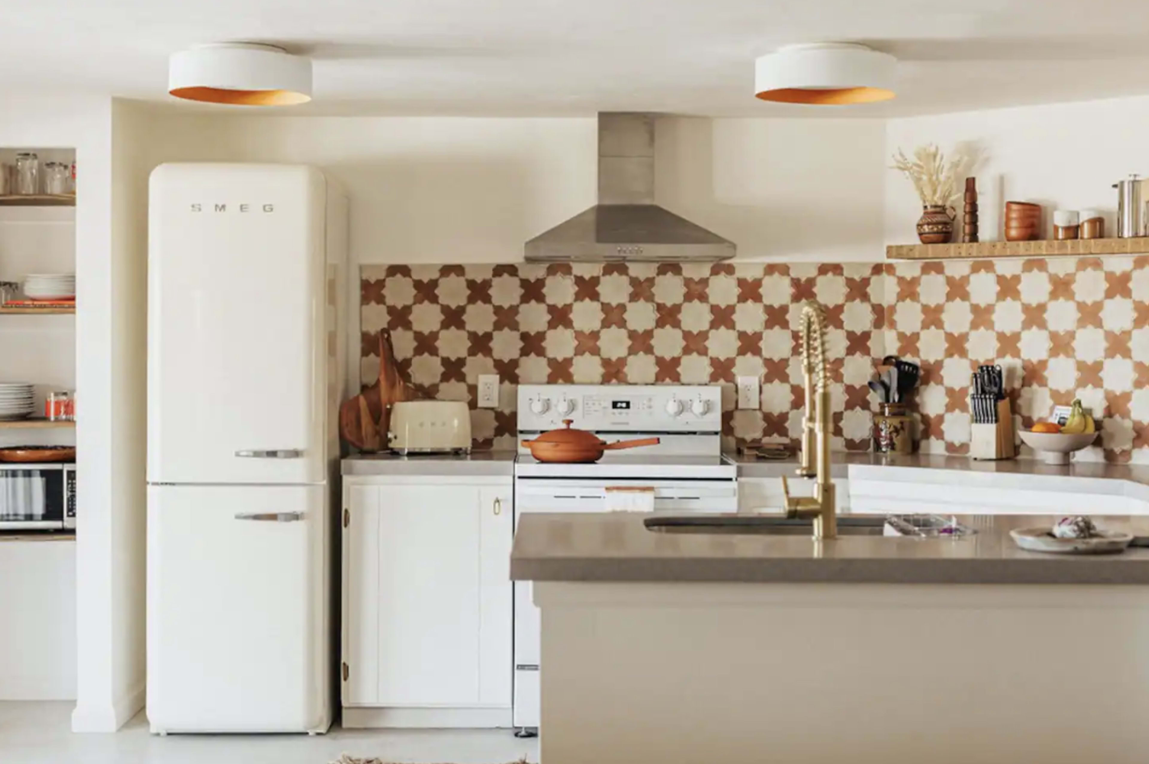 A modern kitchen features a white SMEG refrigerator, a gas stove, and a decorative tile backsplash, with an open shelving unit displaying various kitchen items.