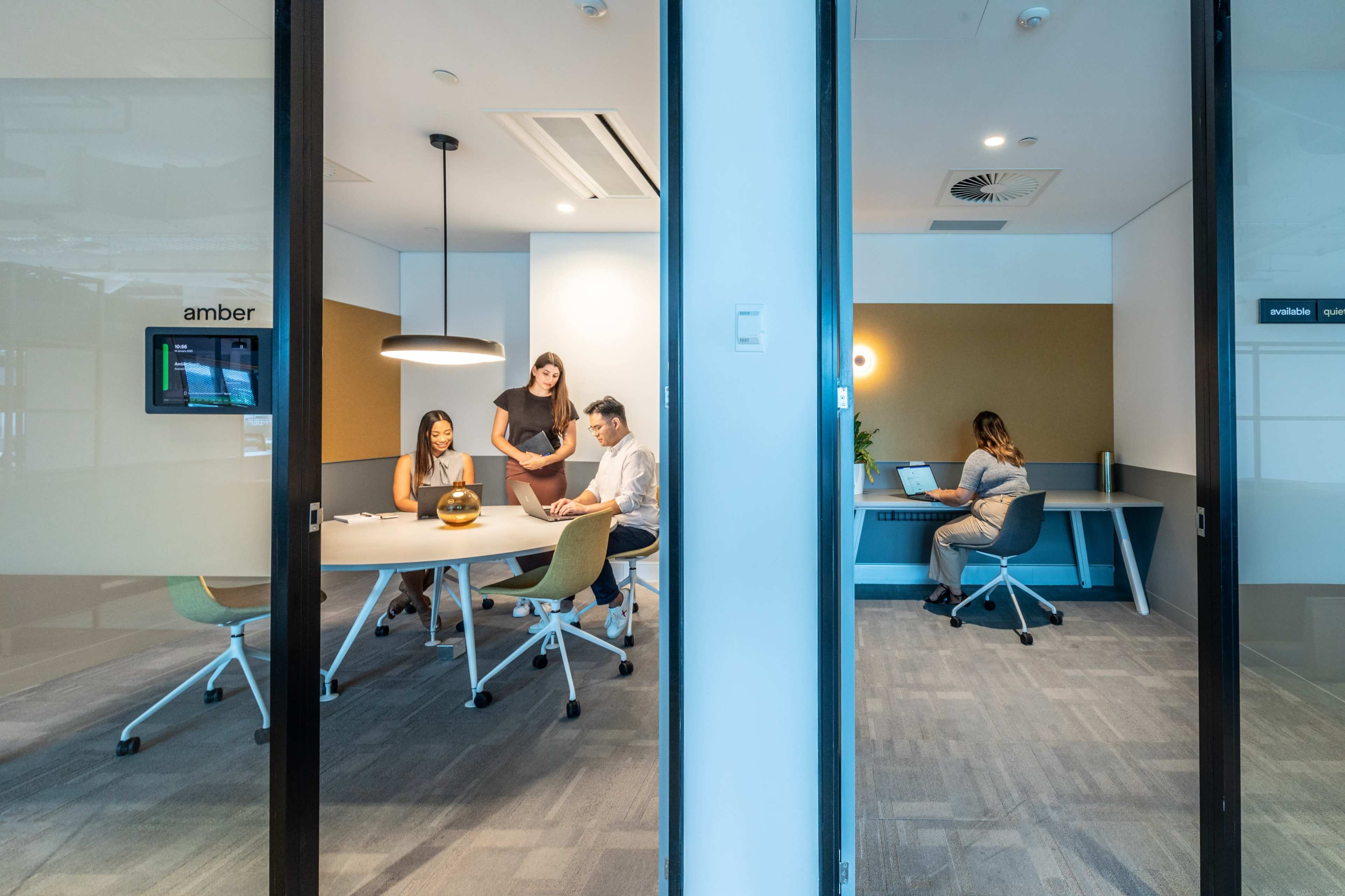 Two office spaces: one containing four people collaborating around a table, and another with a single person working at a desk.
