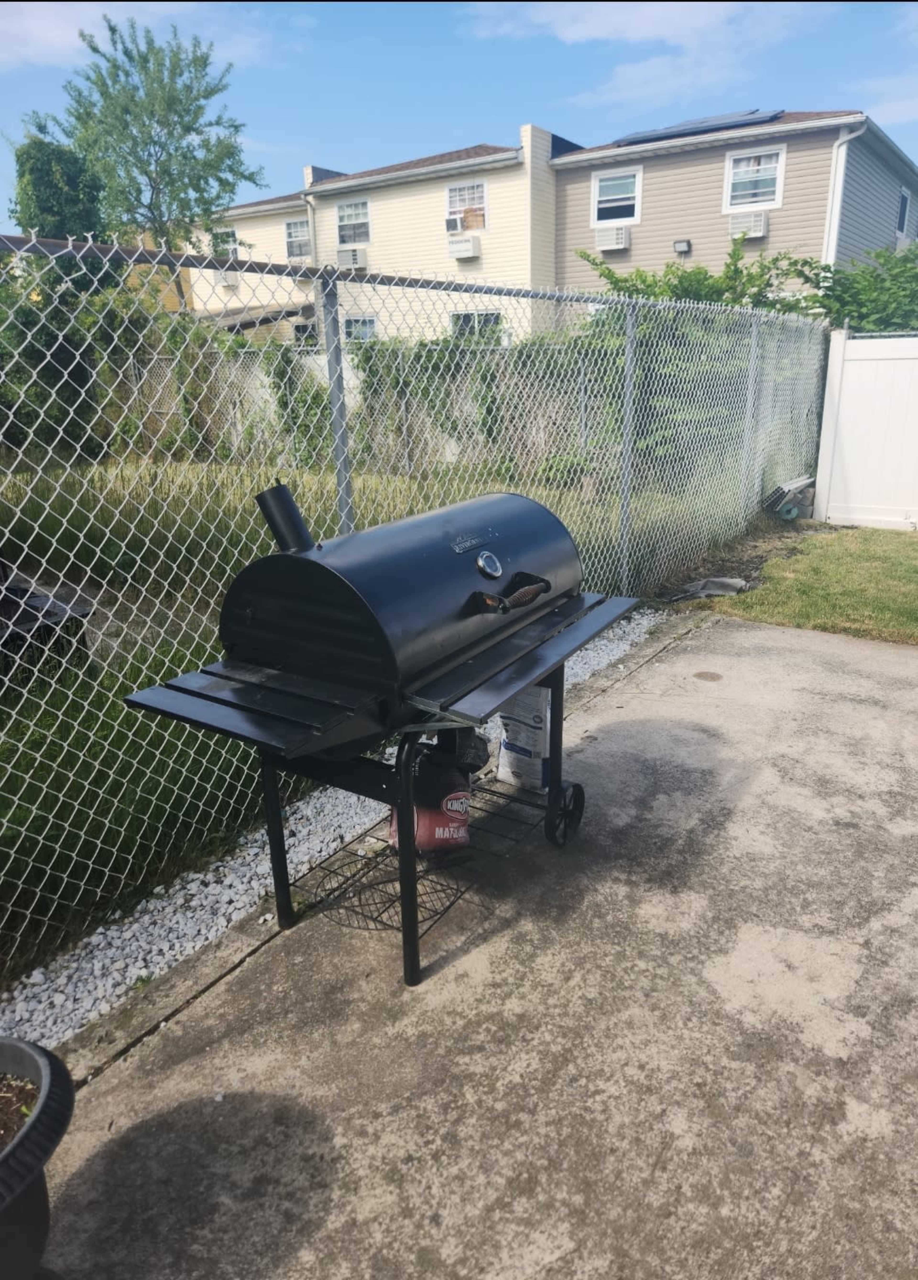 A black barbecue grill is positioned on a concrete patio next to a fenced backyard.