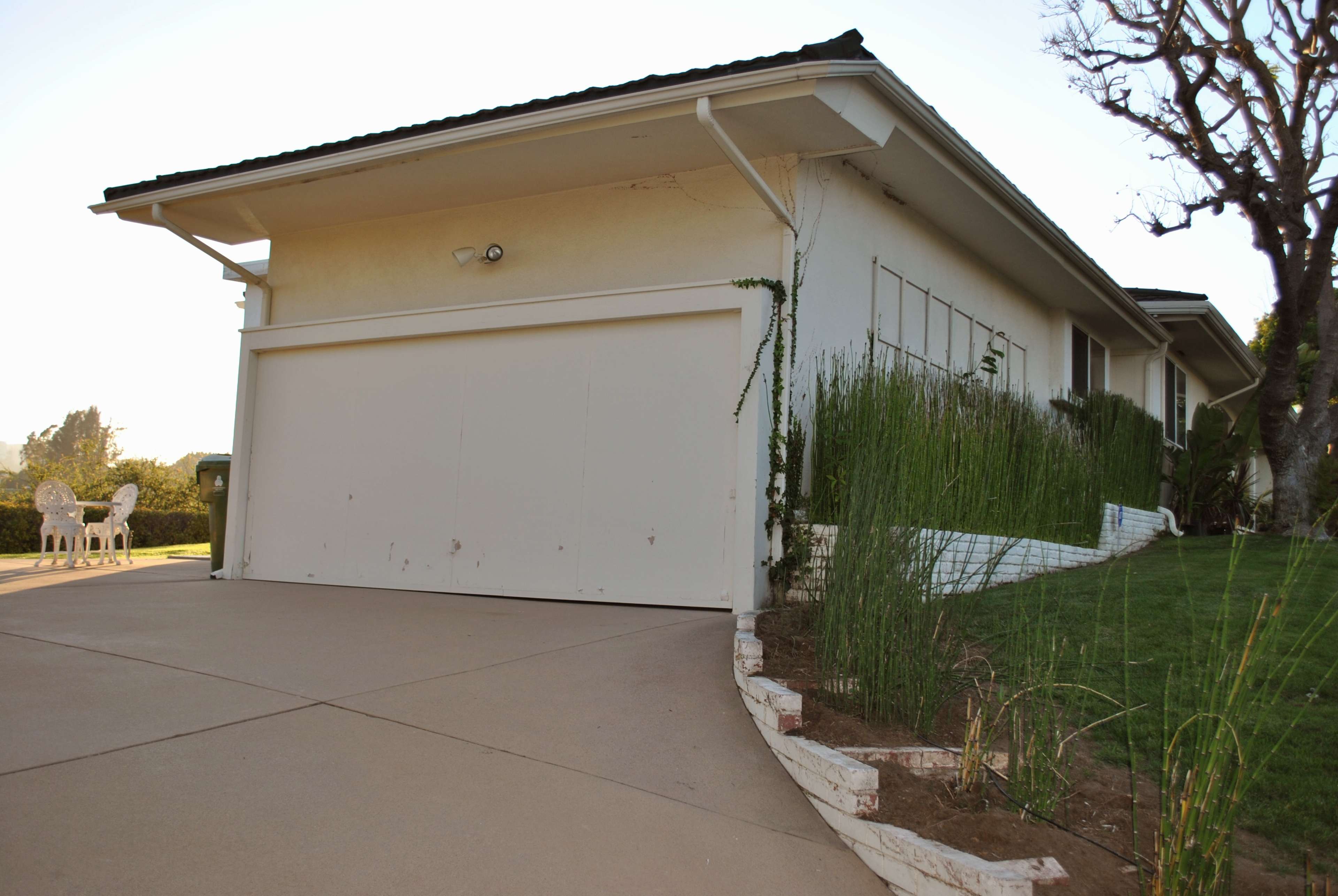A house with a white garage door, surrounded by a neatly manicured lawn and a small garden along the pathway.
