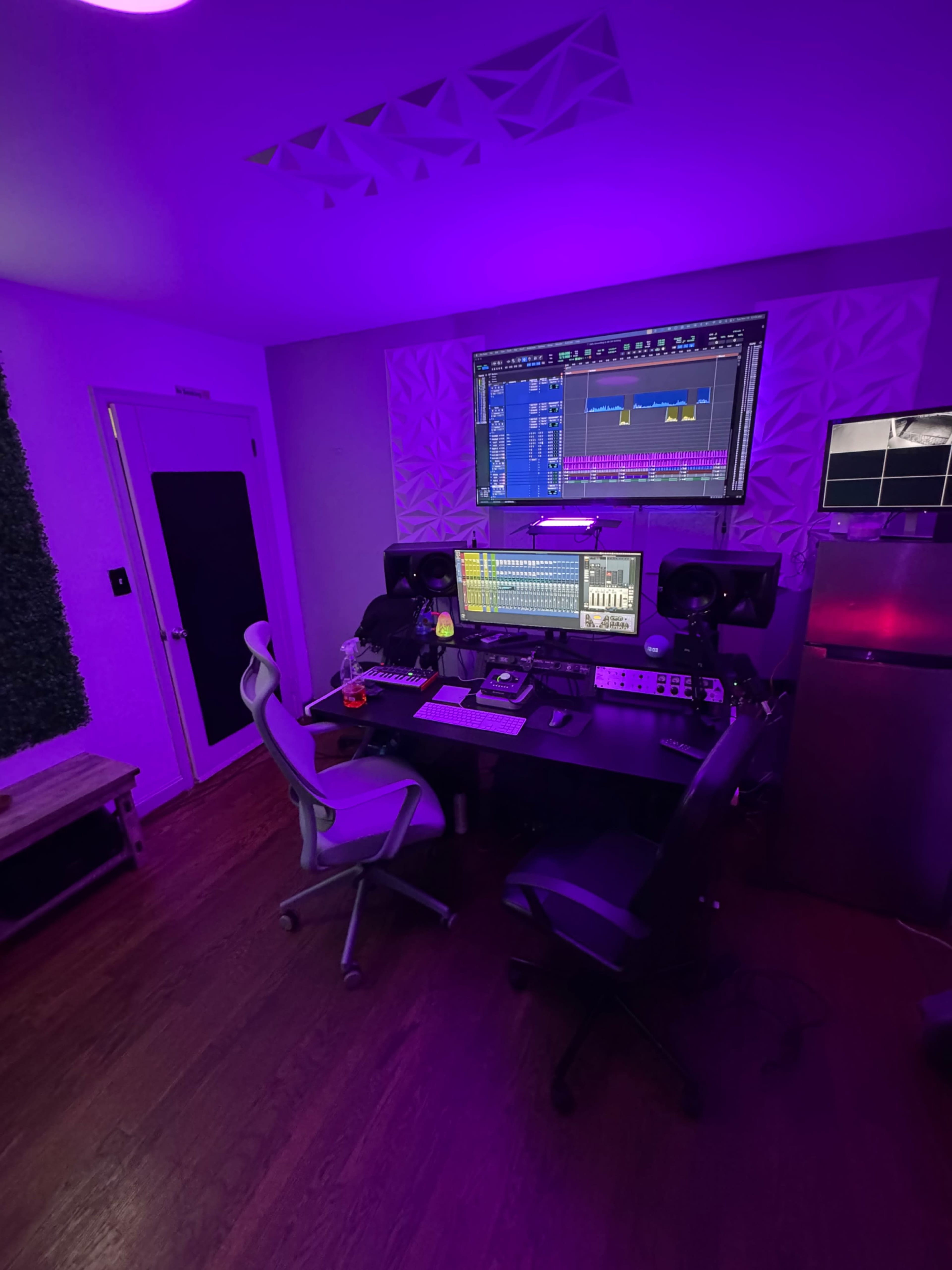 The image depicts a music production studio featuring a desk with computer monitors, audio equipment, and purple ambient lighting.