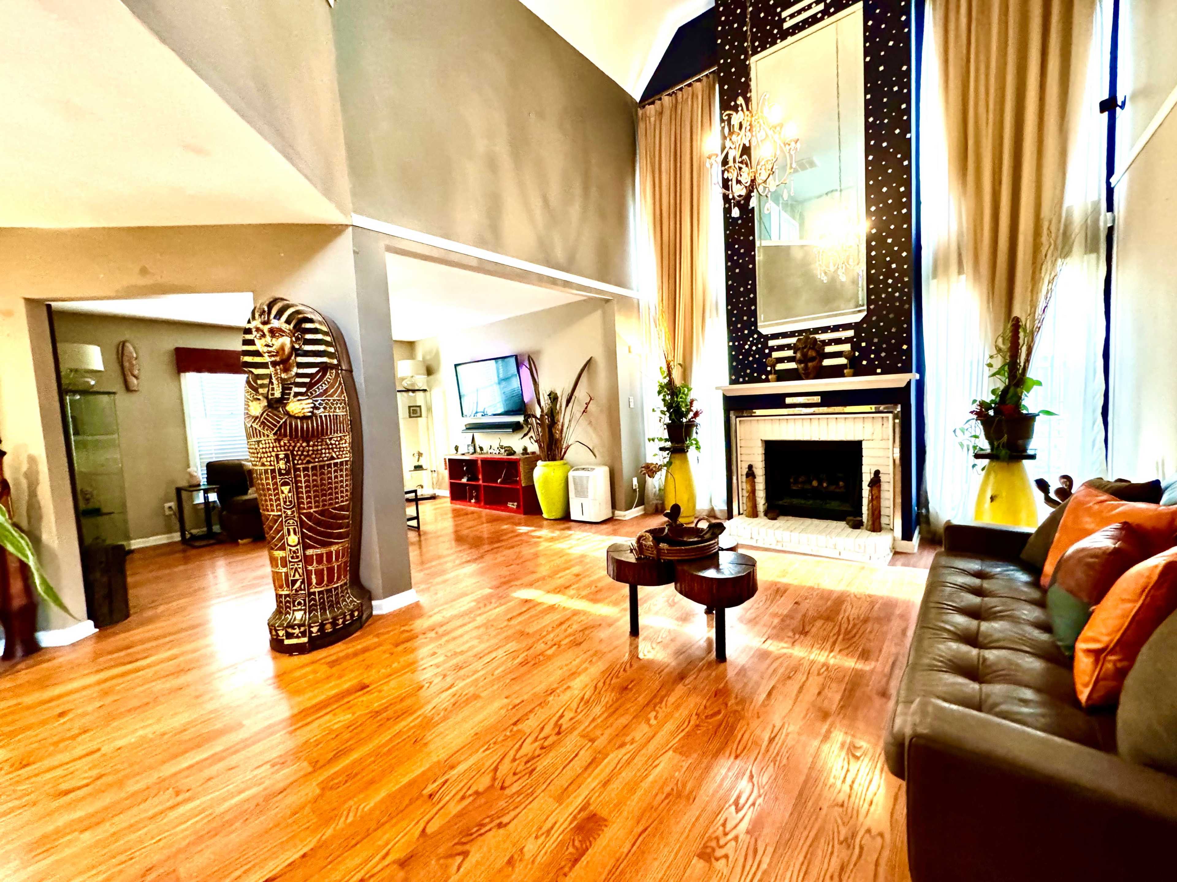 A spacious living room featuring hardwood floors, a large mirror, a decorative fireplace, and a golden Egyptian-style statue.