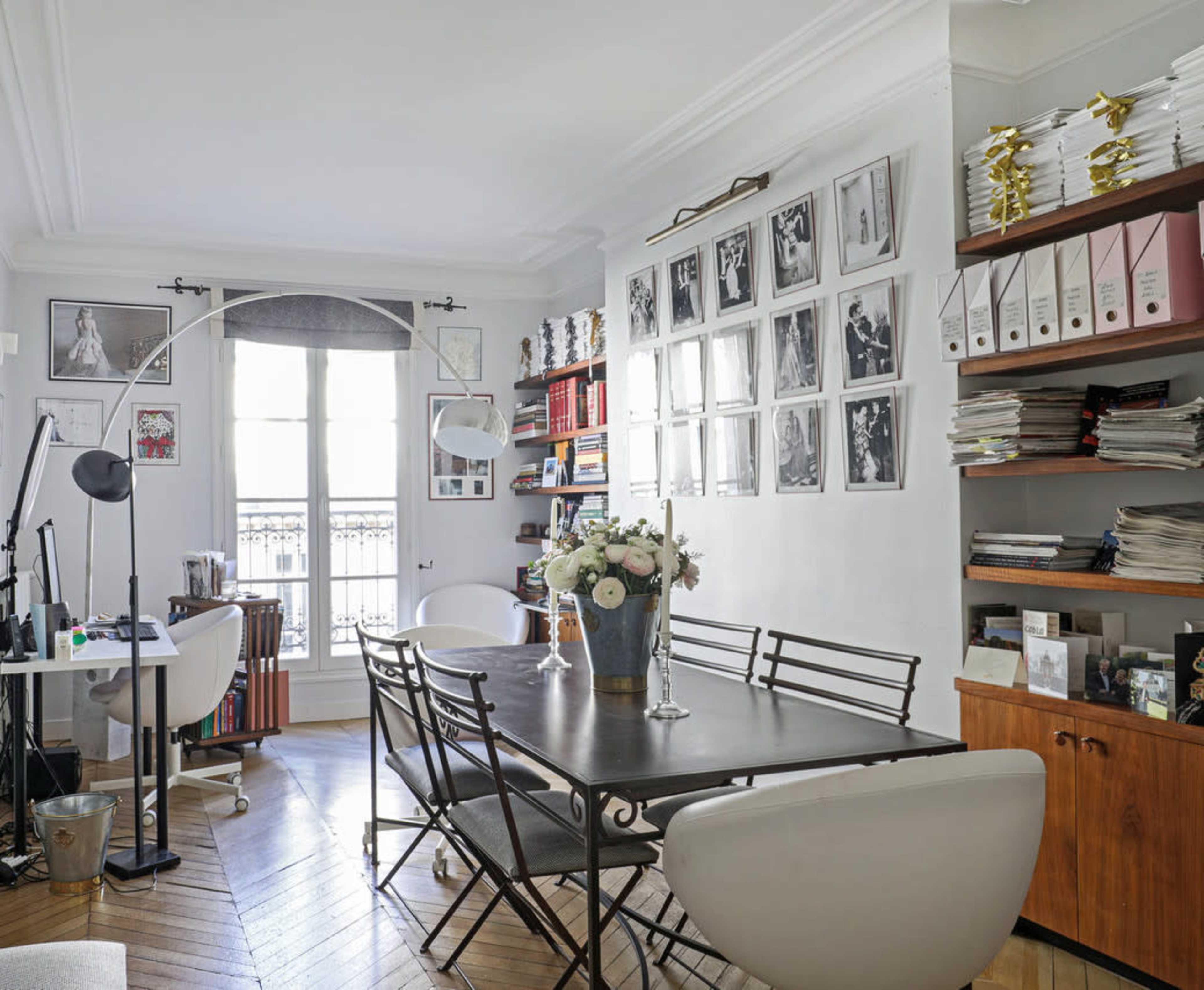 A well-organized office features a large table surrounded by chairs, shelves filled with binders and books, and large windows allowing natural light to illuminate the space.