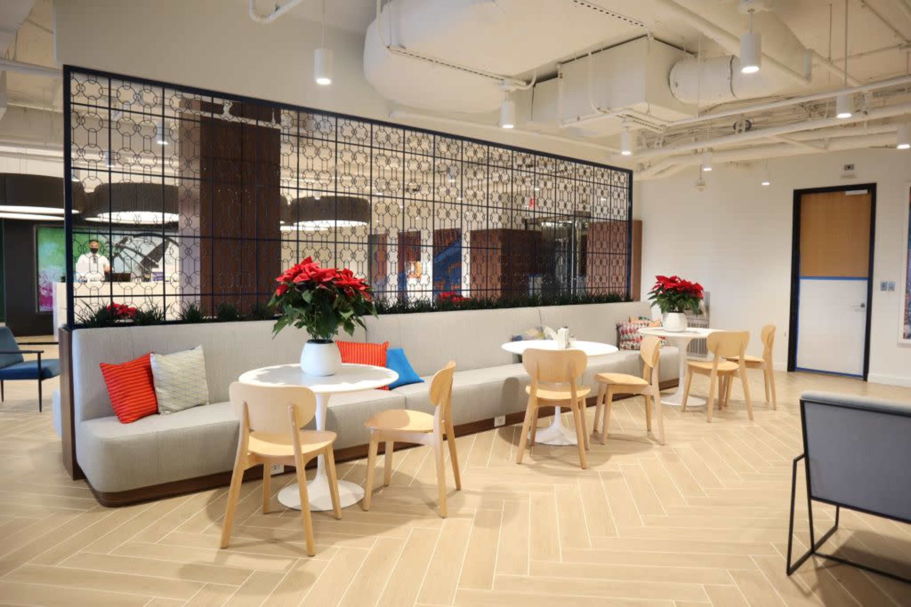 A modern lounge area with a seating arrangement that includes a long couch and small round tables, adorned with festive red poinsettias.