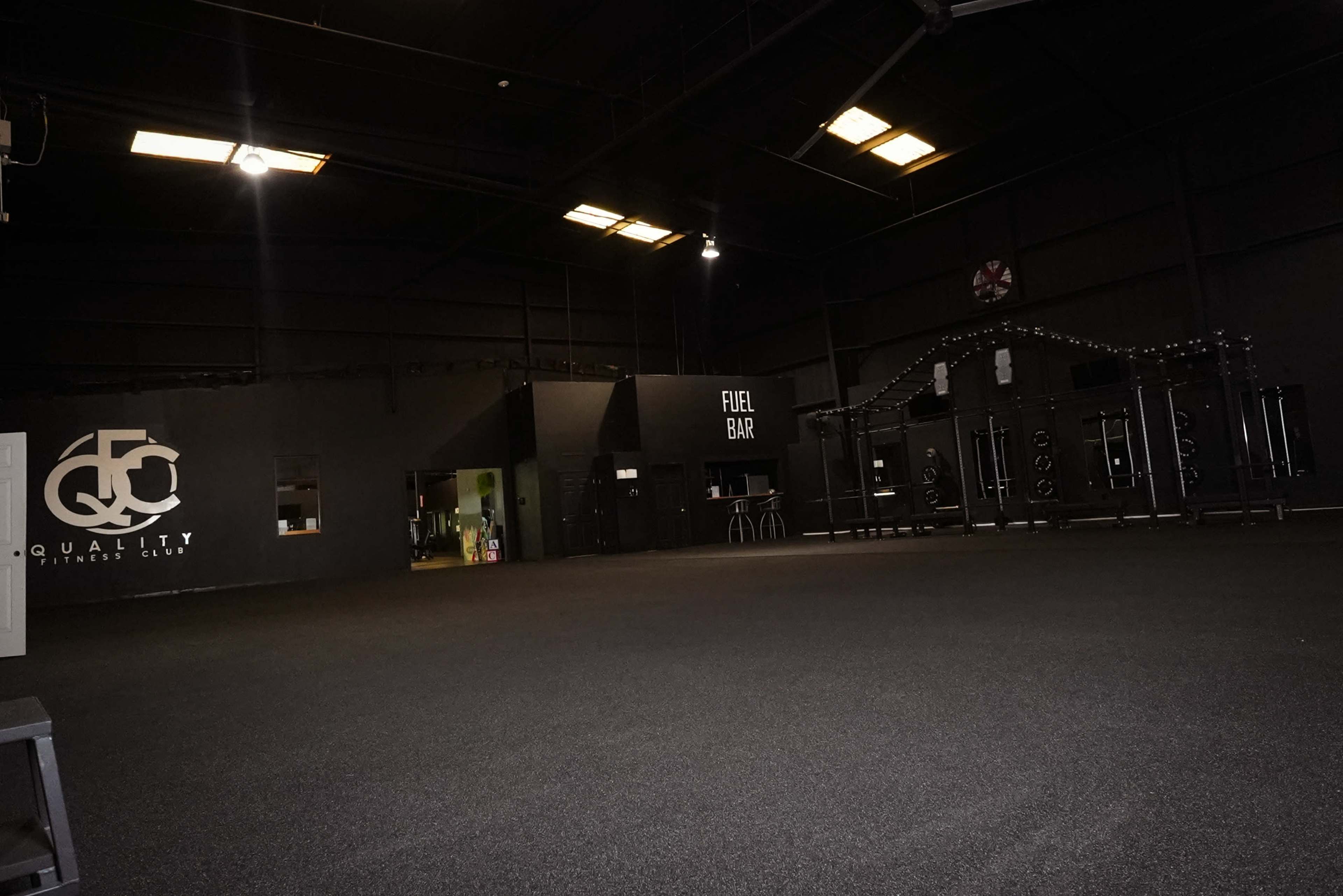 The image shows the interior of a gym featuring black walls, a spacious area with rubber flooring, and a fuel bar on one side.