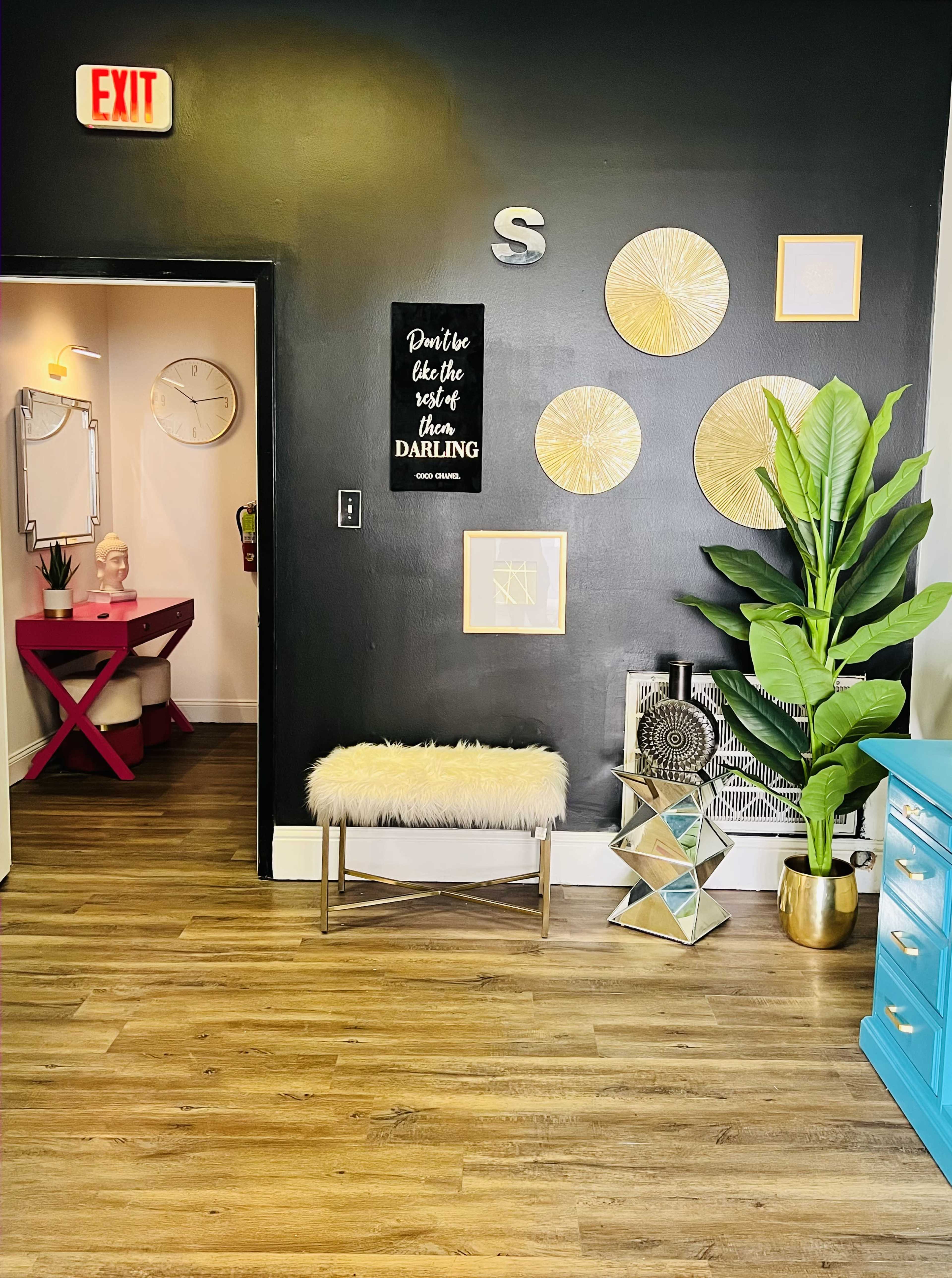 The image shows an interior space featuring a black wall, a decorative bench with a furry top, round wall decorations, and a large green plant beside a colorful dresser.