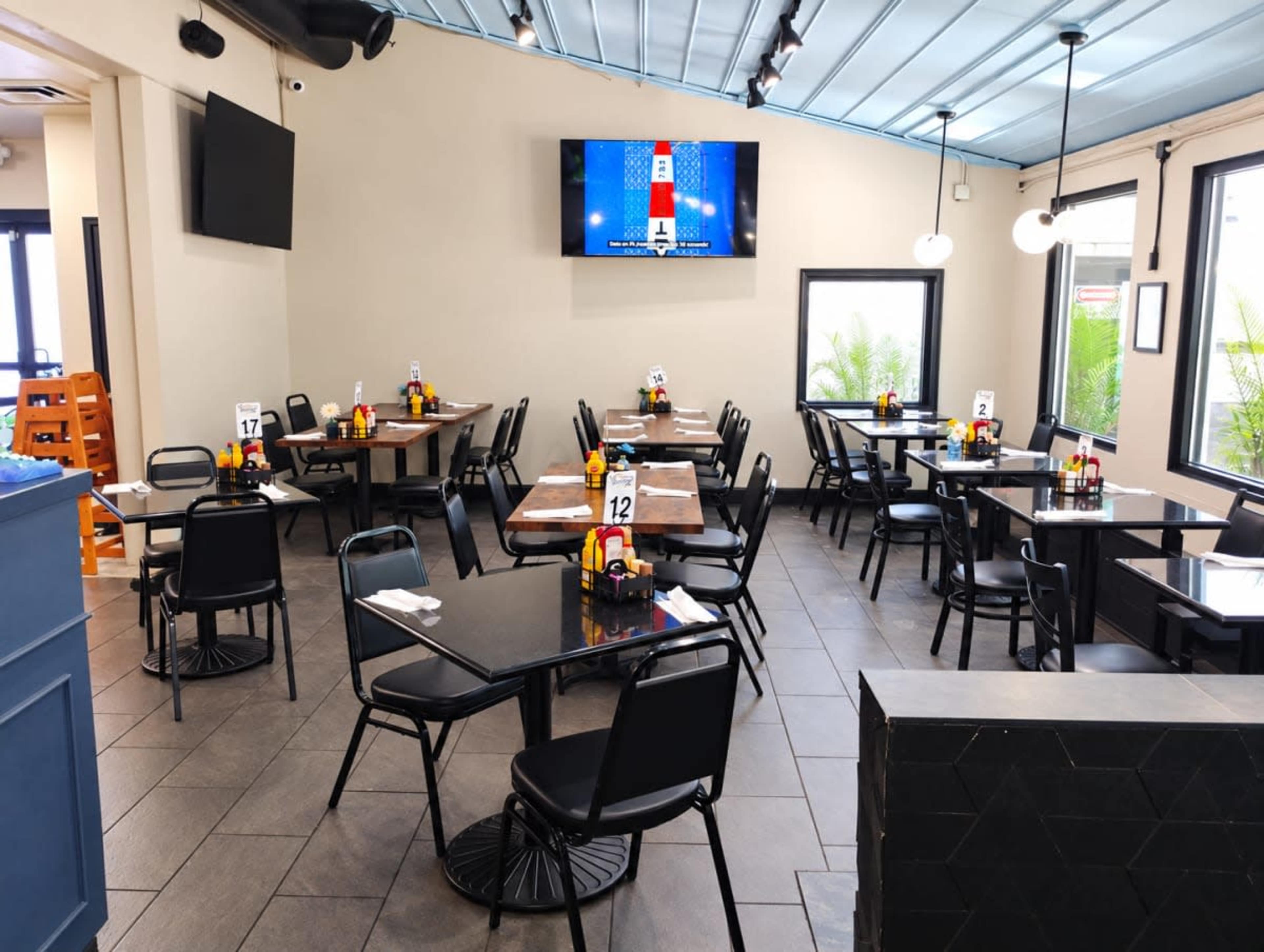 The image shows a brightly lit restaurant interior with several tables set for dining, featuring black chairs and numbered table markers.