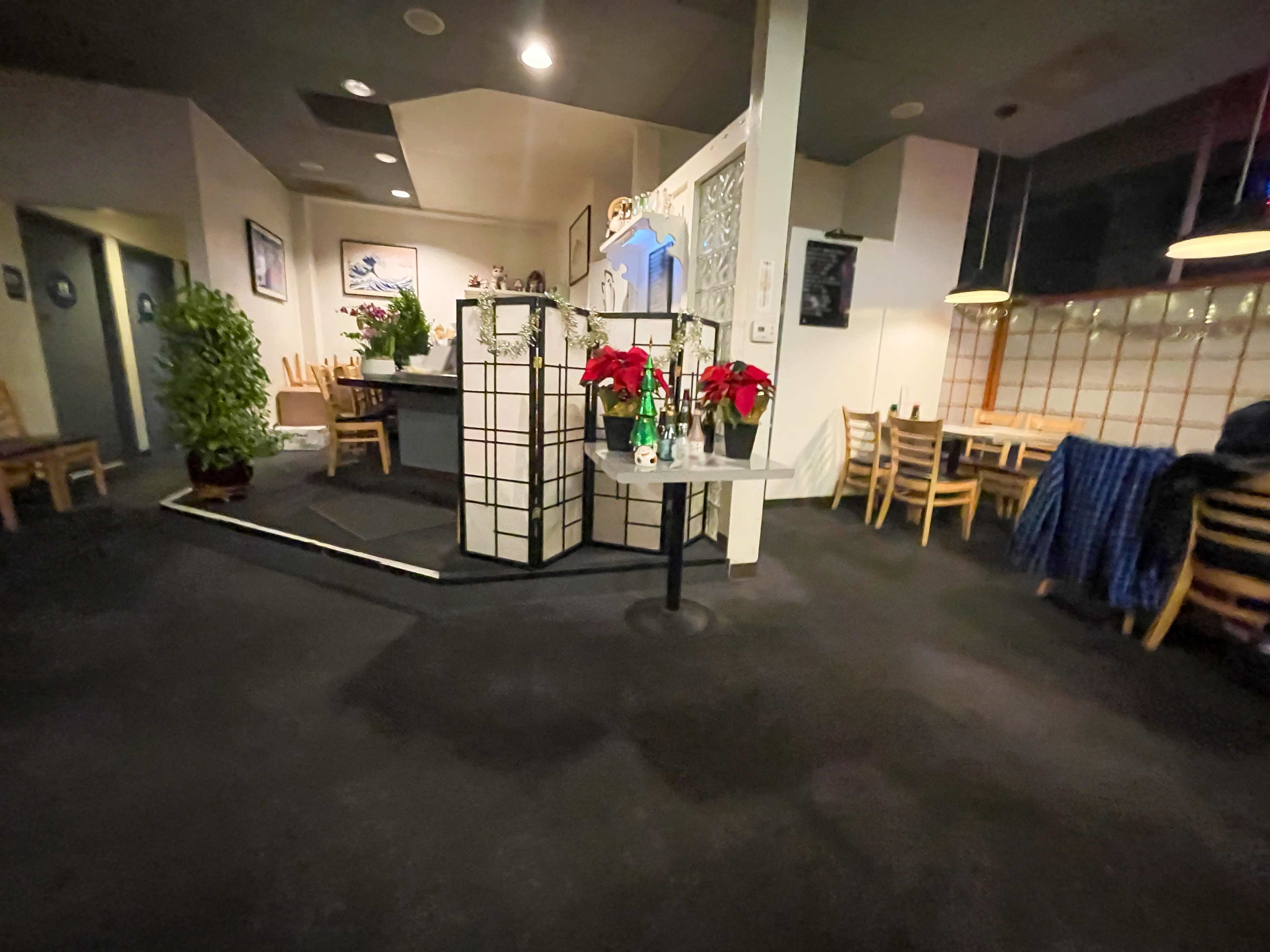 The image shows the interior of a restaurant, featuring a reception area with a small divider and seating arrangements on the side.