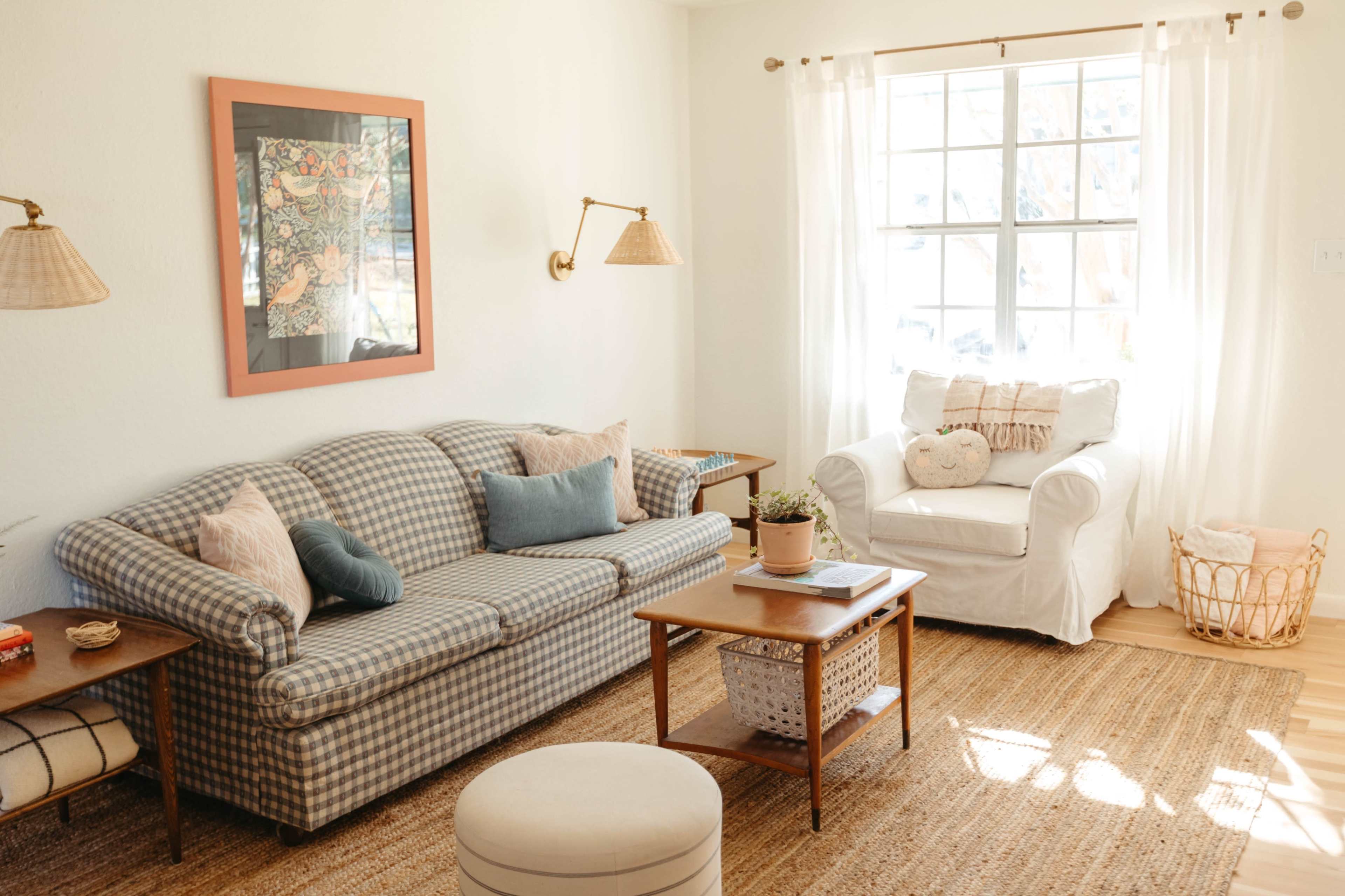 A cozy living room features a patterned sofa, a white armchair, and a wooden coffee table, with natural light streaming in through a large window.