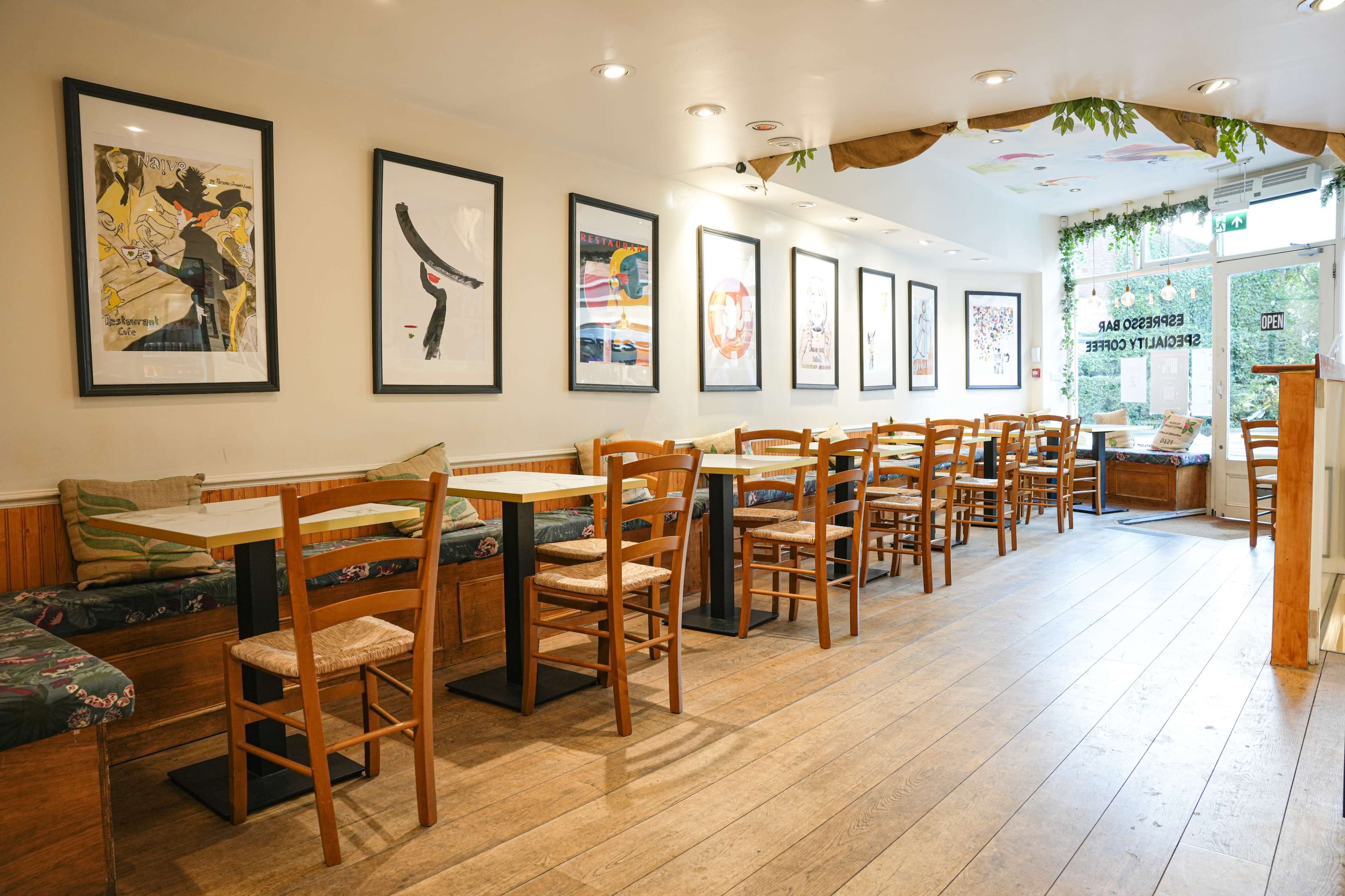 A cafe interior with wooden floors, lined with tables and chairs, and walls adorned with framed artwork.