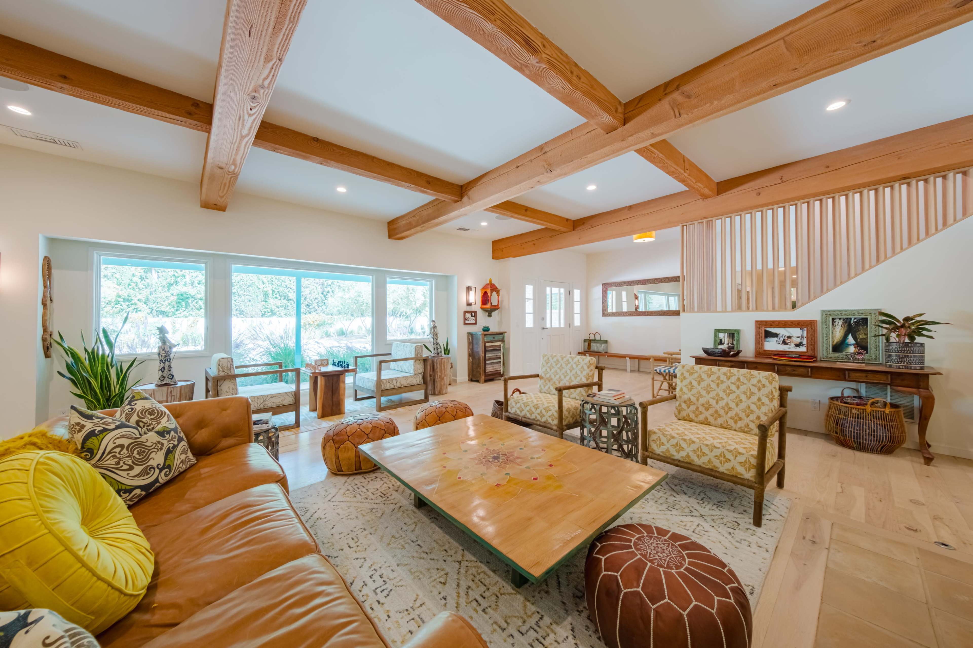 A spacious living room with wooden beams on the ceiling, a large coffee table, and various seating arrangements featuring a mix of cushions and patterned chairs.
