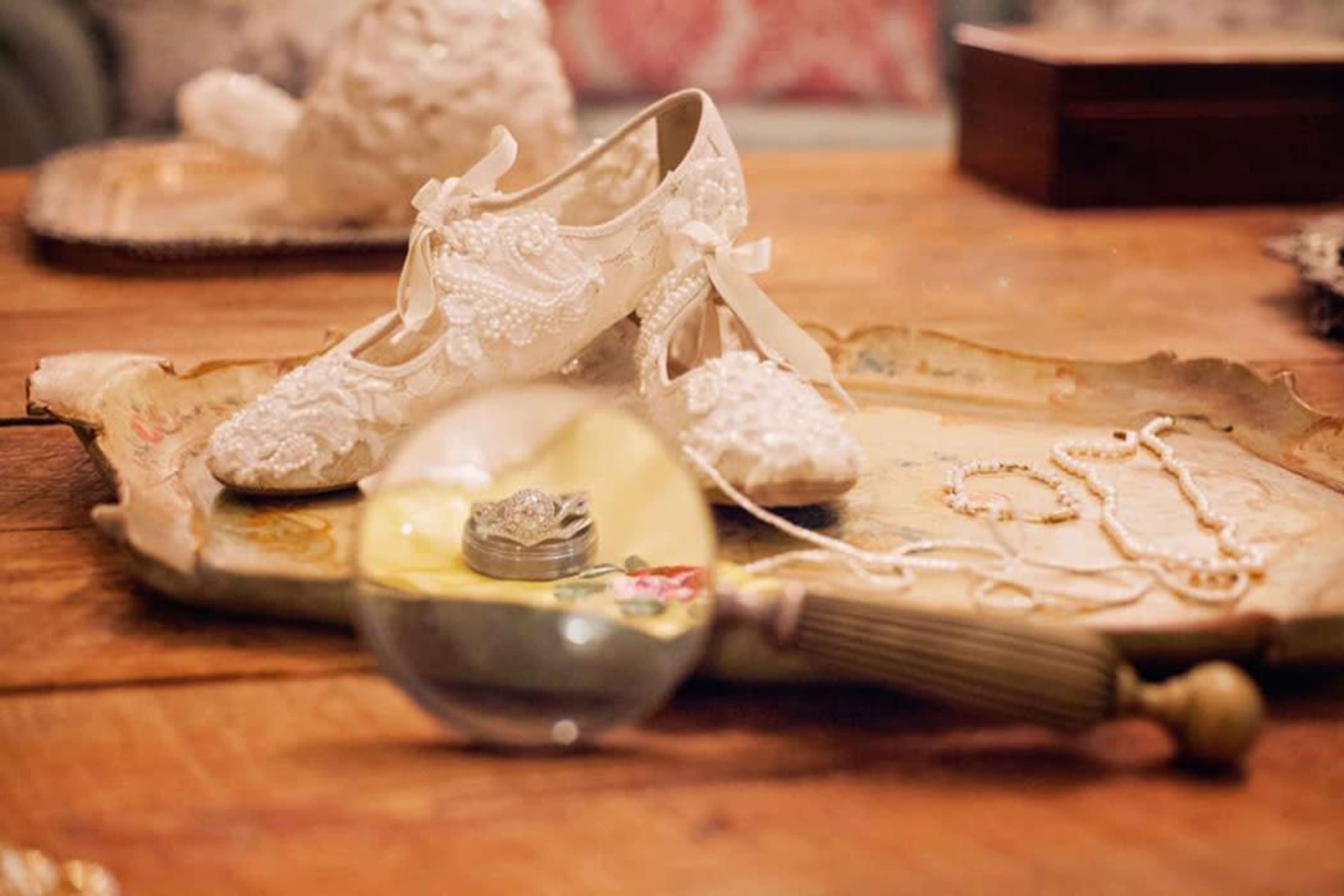 A pair of intricately designed wedding shoes rests on a decorative tray next to a jewelry box and a necklace.