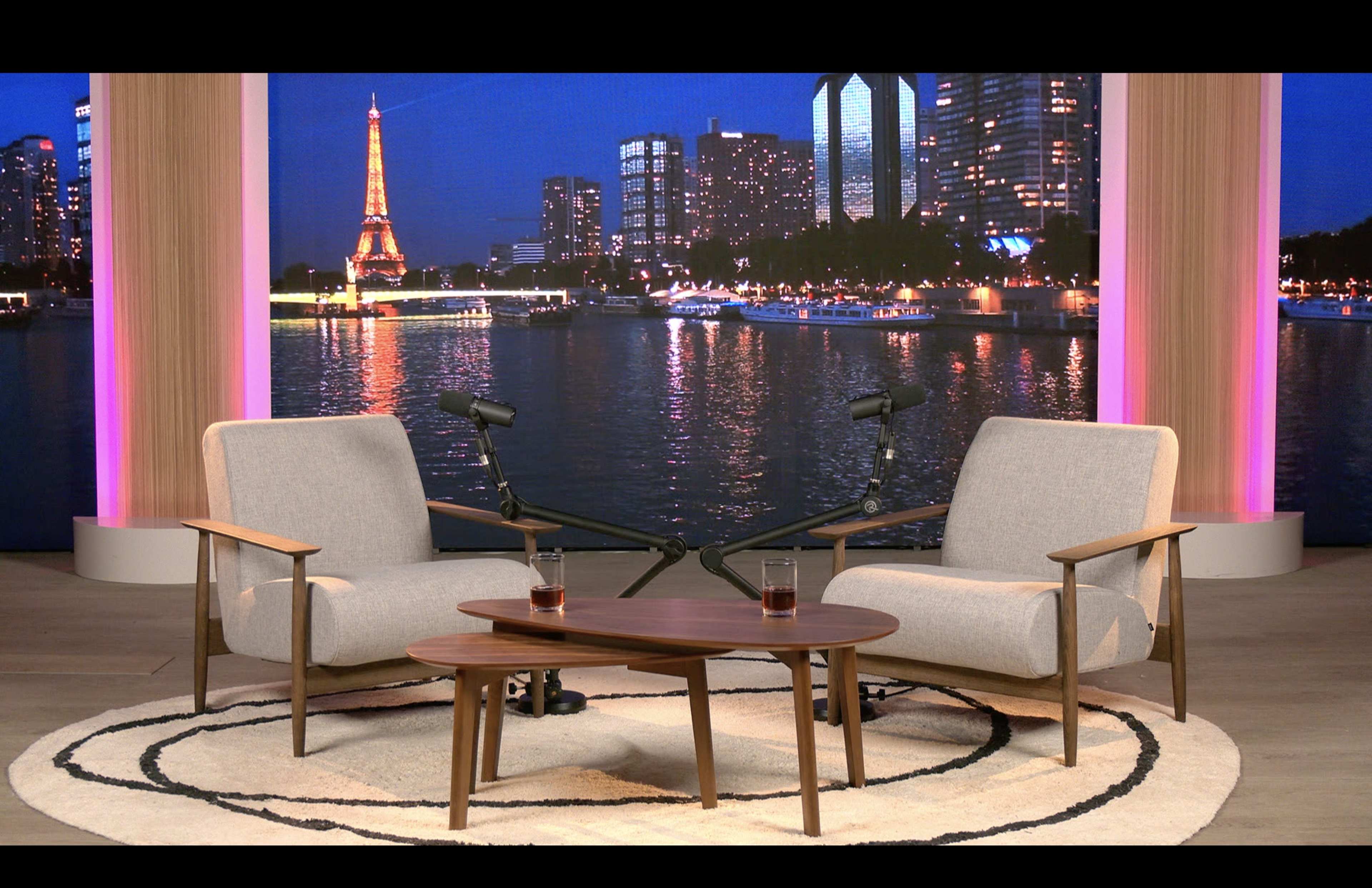 The scene features two modern armchairs and a low coffee table set against a background of a city skyline with the Eiffel Tower illuminated at night.