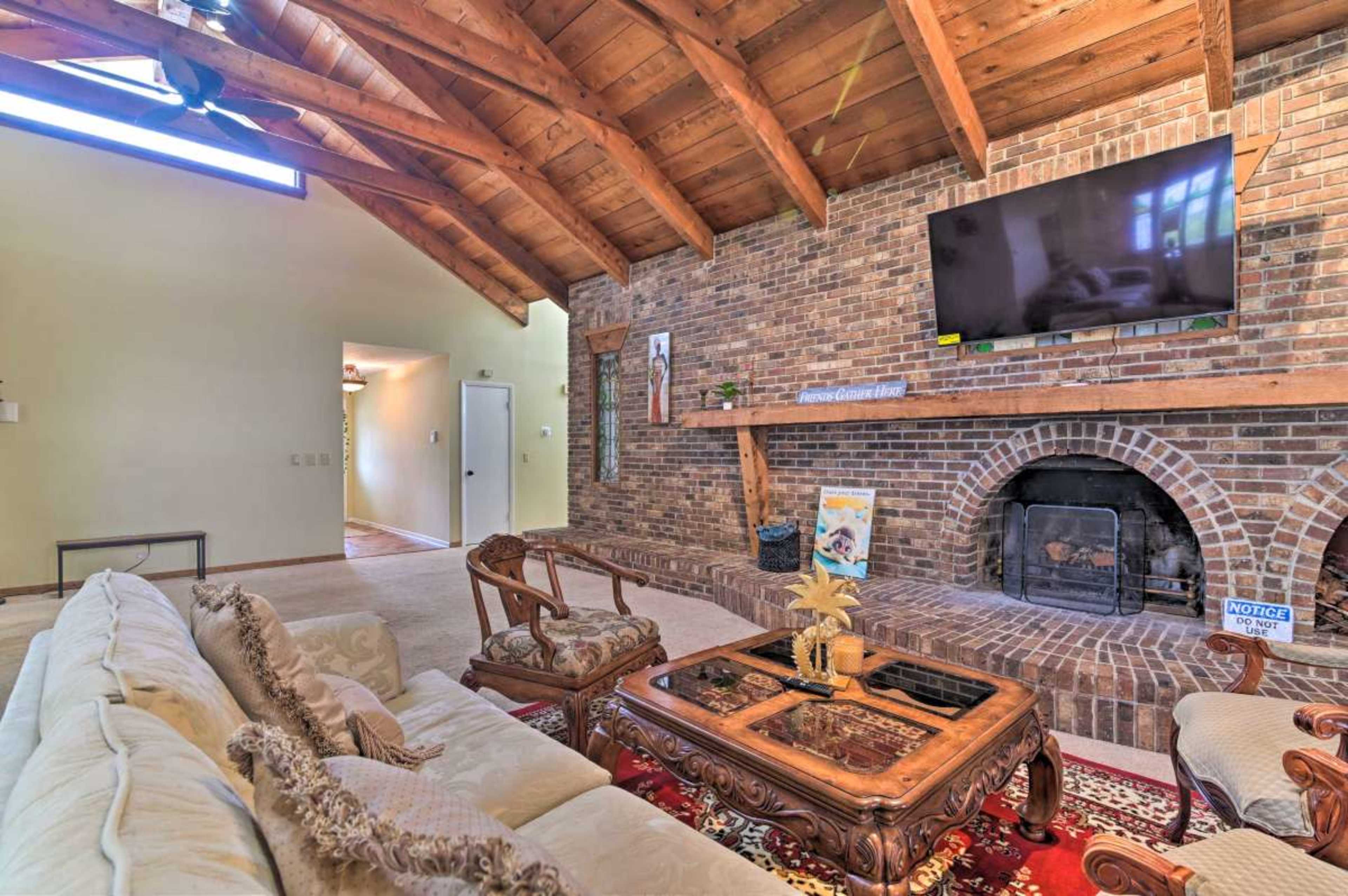 The living room features a beige sofa, a wooden coffee table, and a brick fireplace, with a high wooden-beam ceiling and a wall-mounted television.