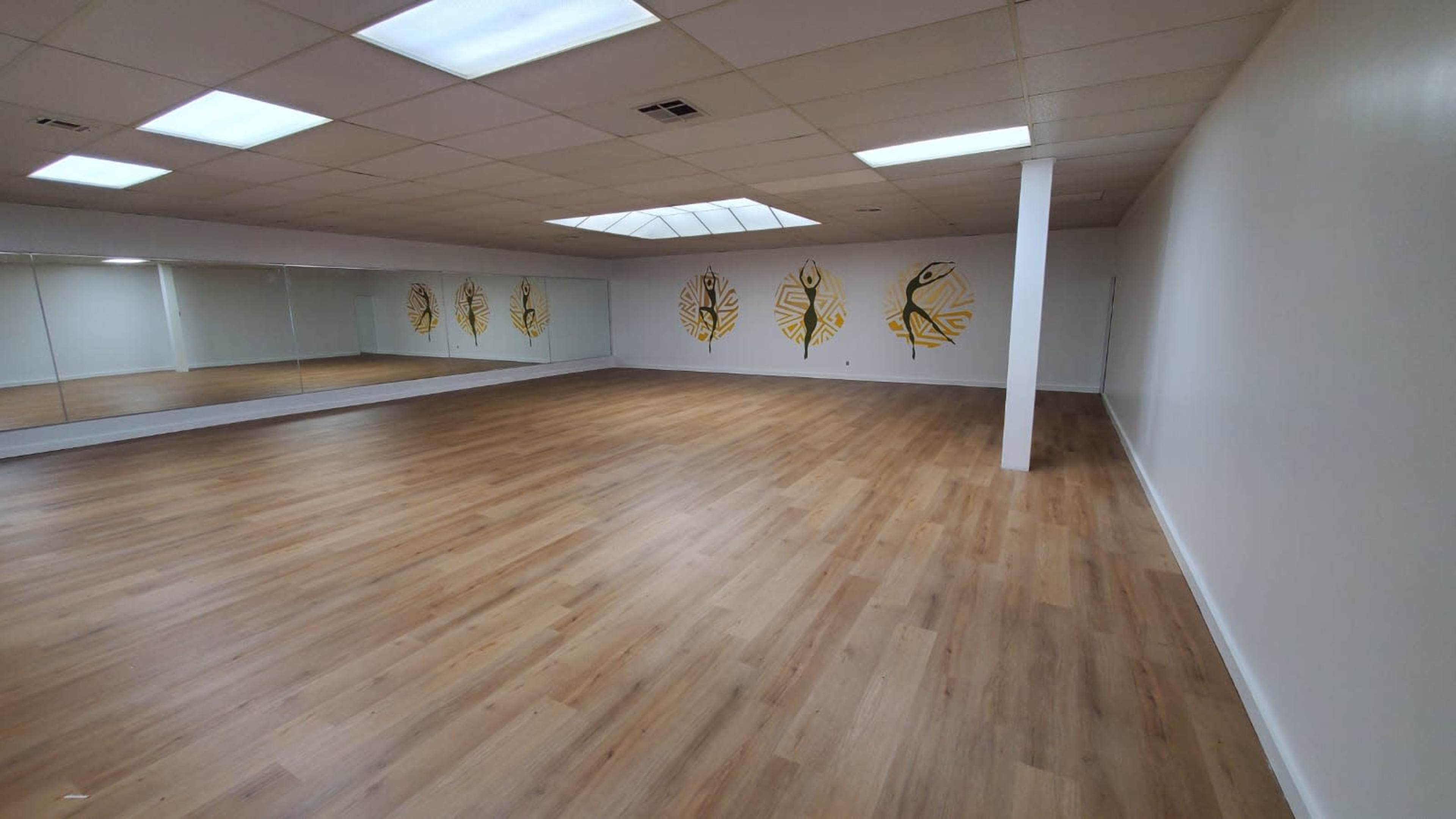 A spacious dance studio features wooden flooring, mirrored walls, and yellow leaf murals.