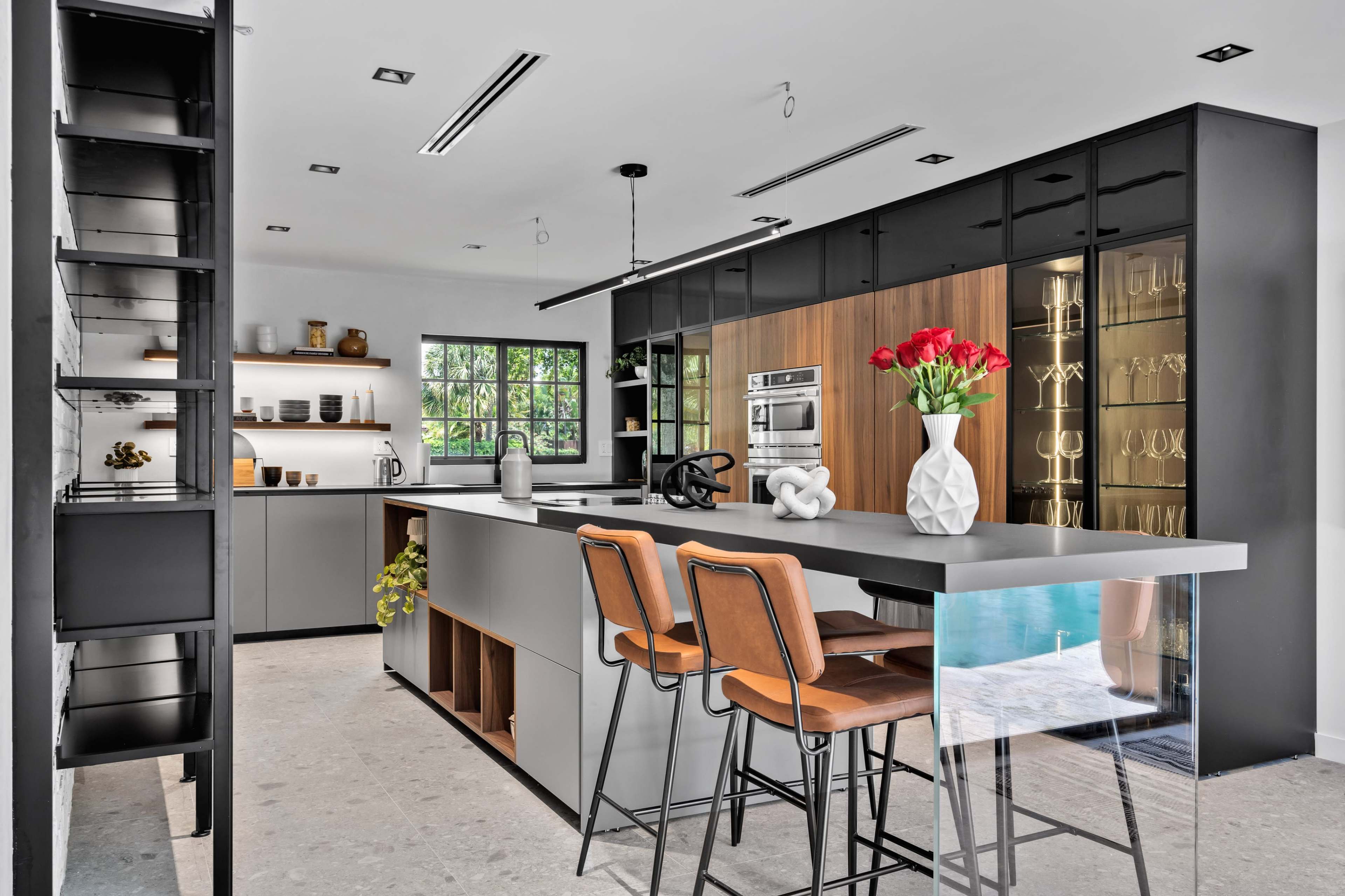 A modern kitchen features sleek cabinetry, an island with bar stools, and large windows providing natural light.