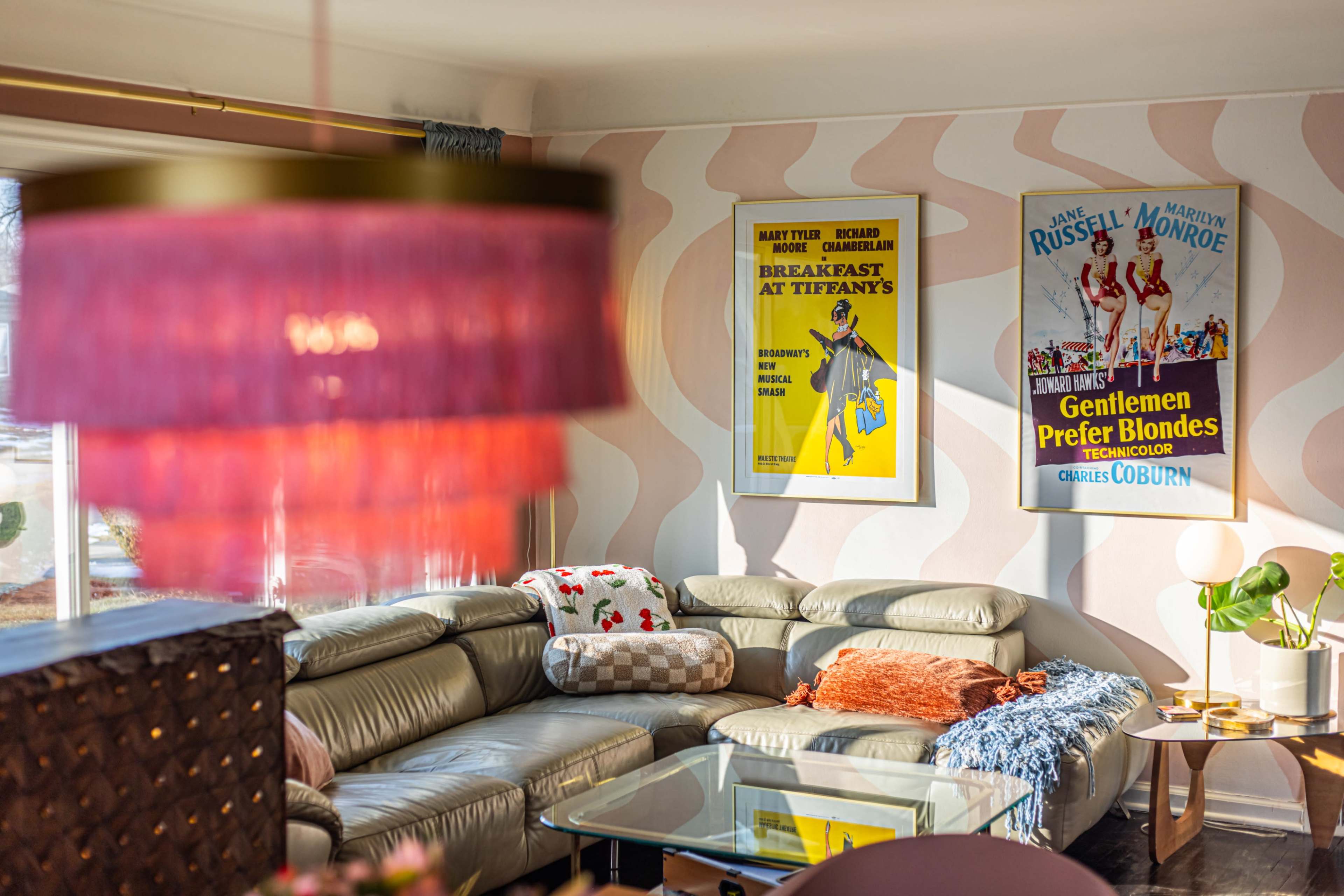 The living room features a curved sectional sofa, a glass coffee table, and two vintage movie posters on patterned walls.