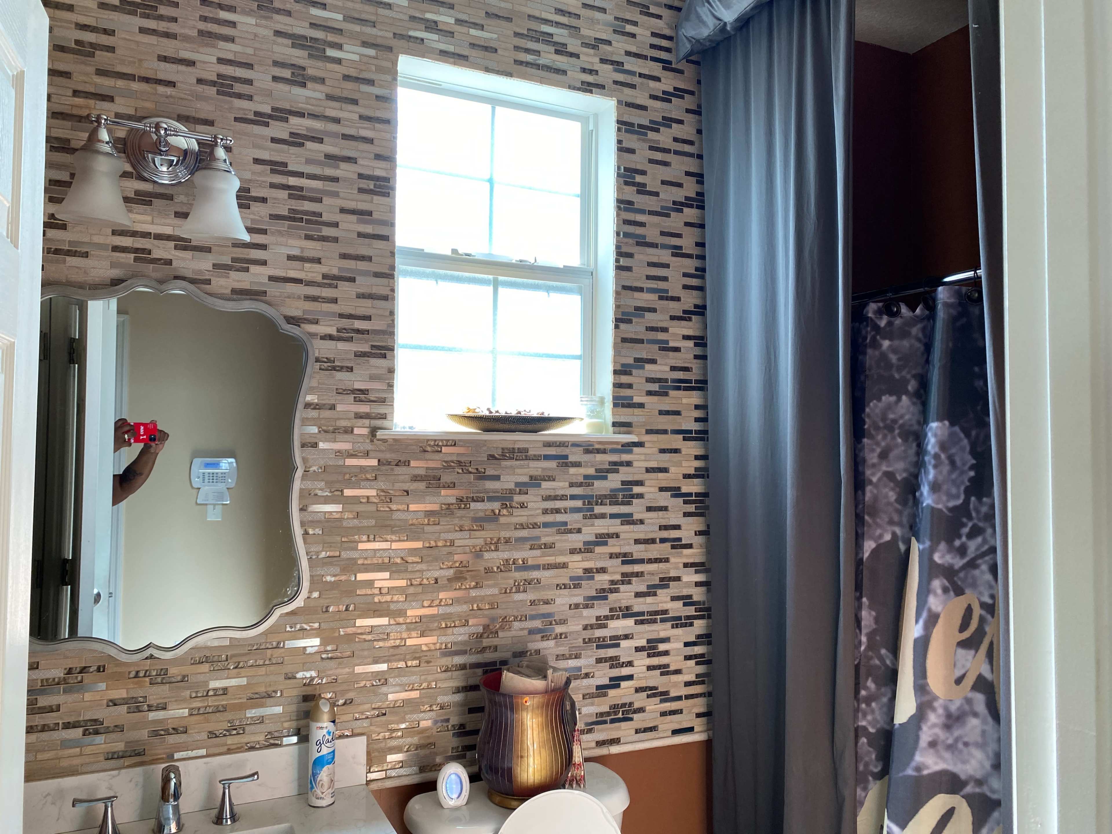 A bathroom featuring a decorative wall with tiles, a mirror, a window, and a shower curtain.