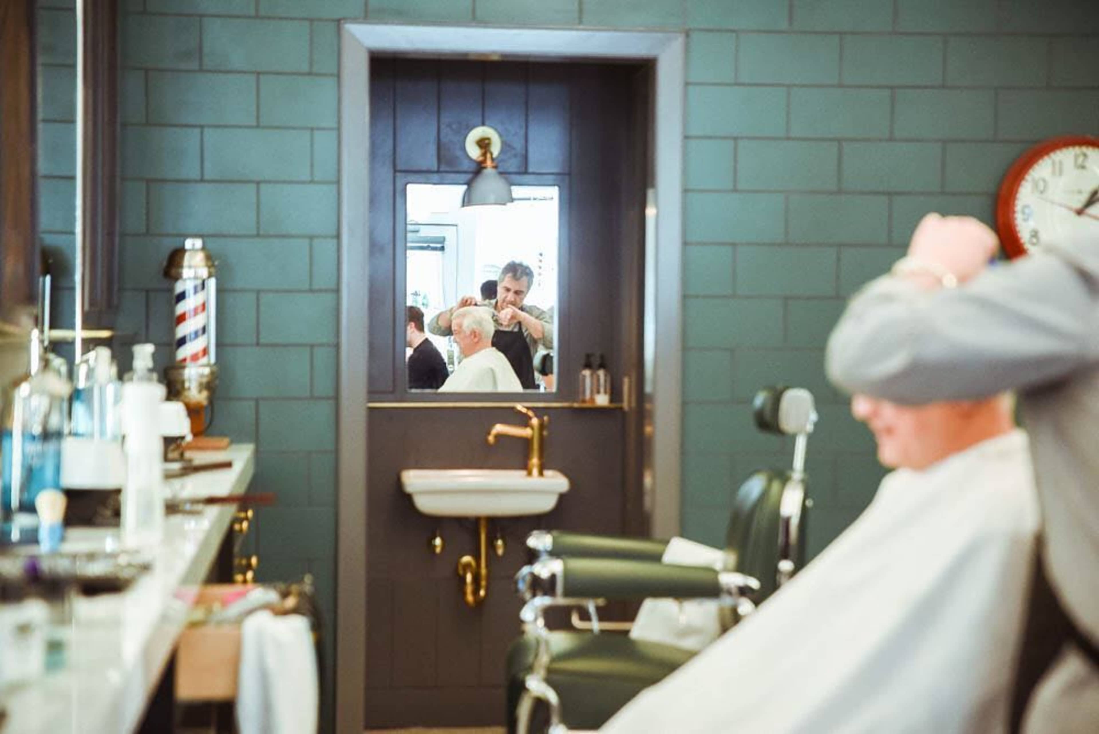 A barber styles a customer's hair in front of a mirror at a barber shop.