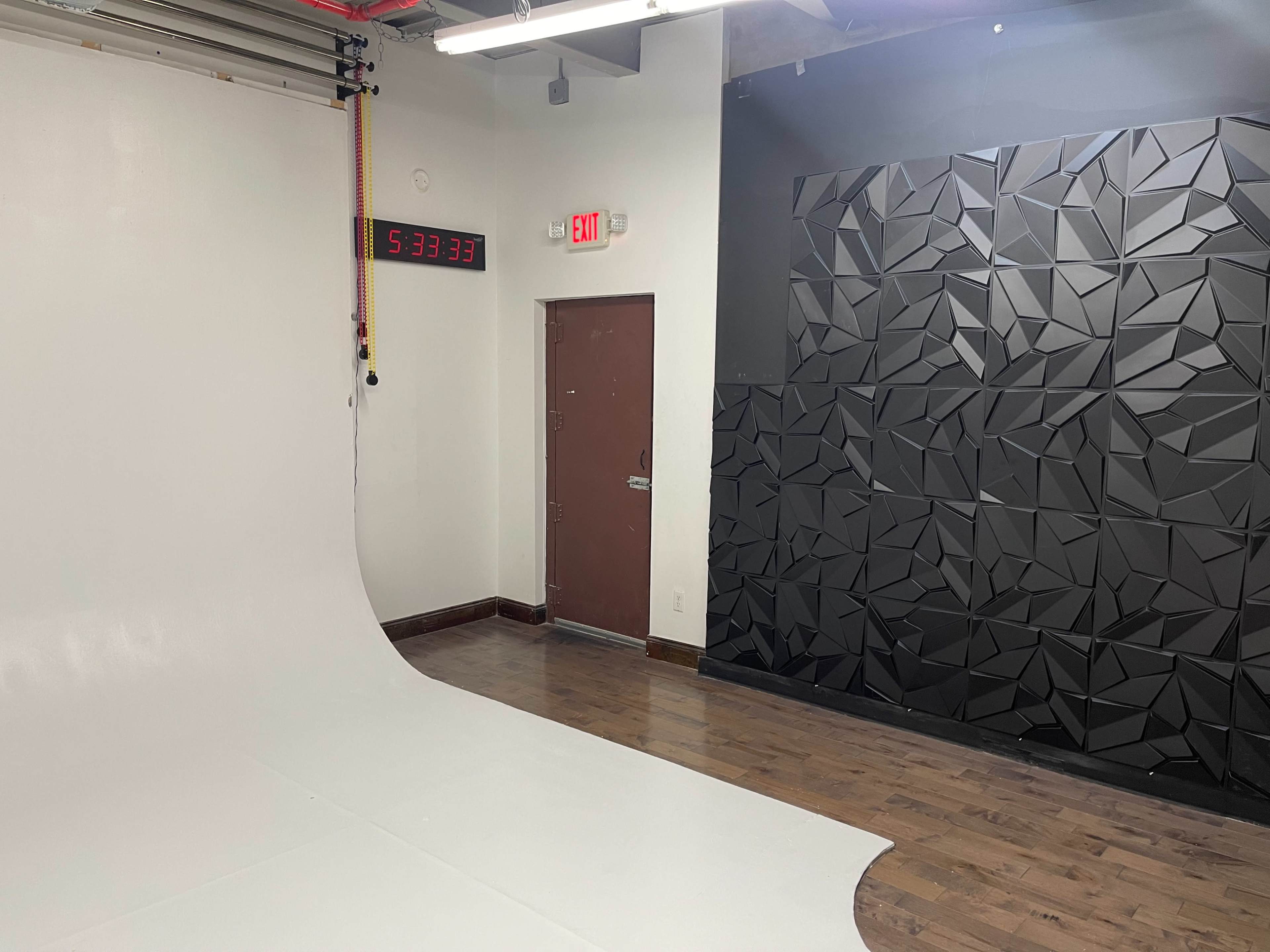 A studio space featuring a curved white backdrop, a wall with a textured black design, and a digital clock displaying the time.