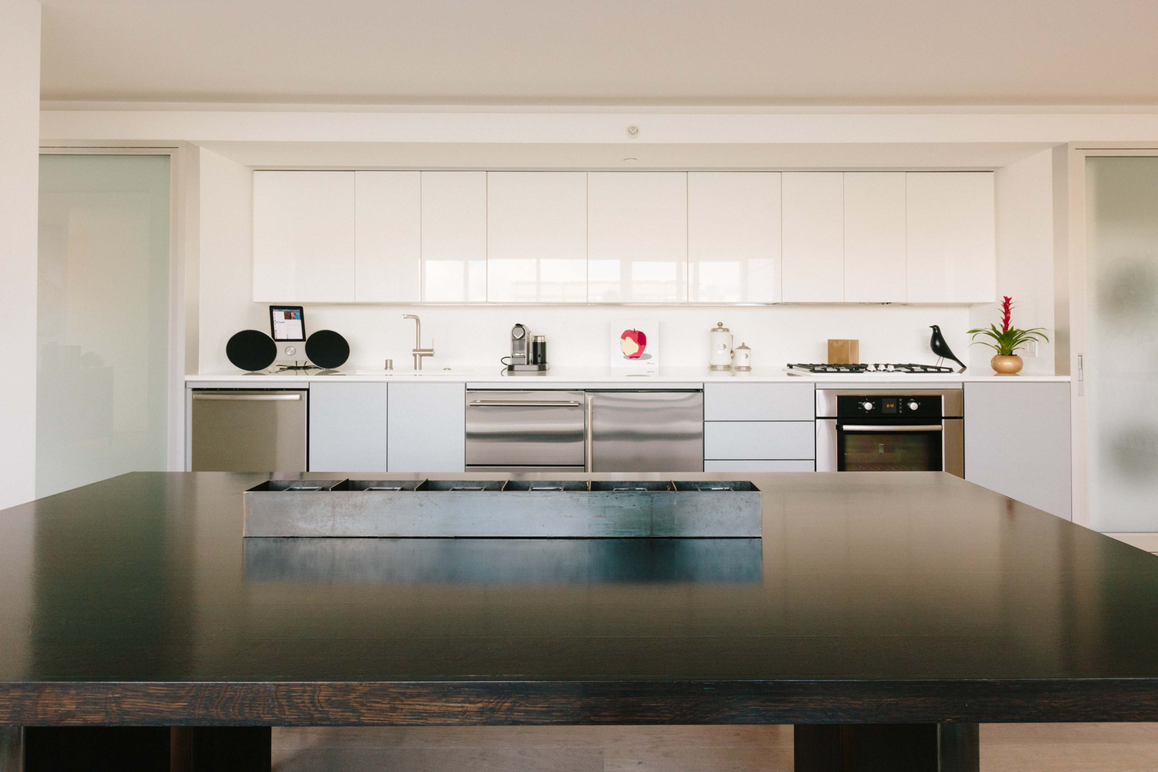 A modern kitchen with white cabinetry, stainless steel appliances, and a large black dining table at the foreground.