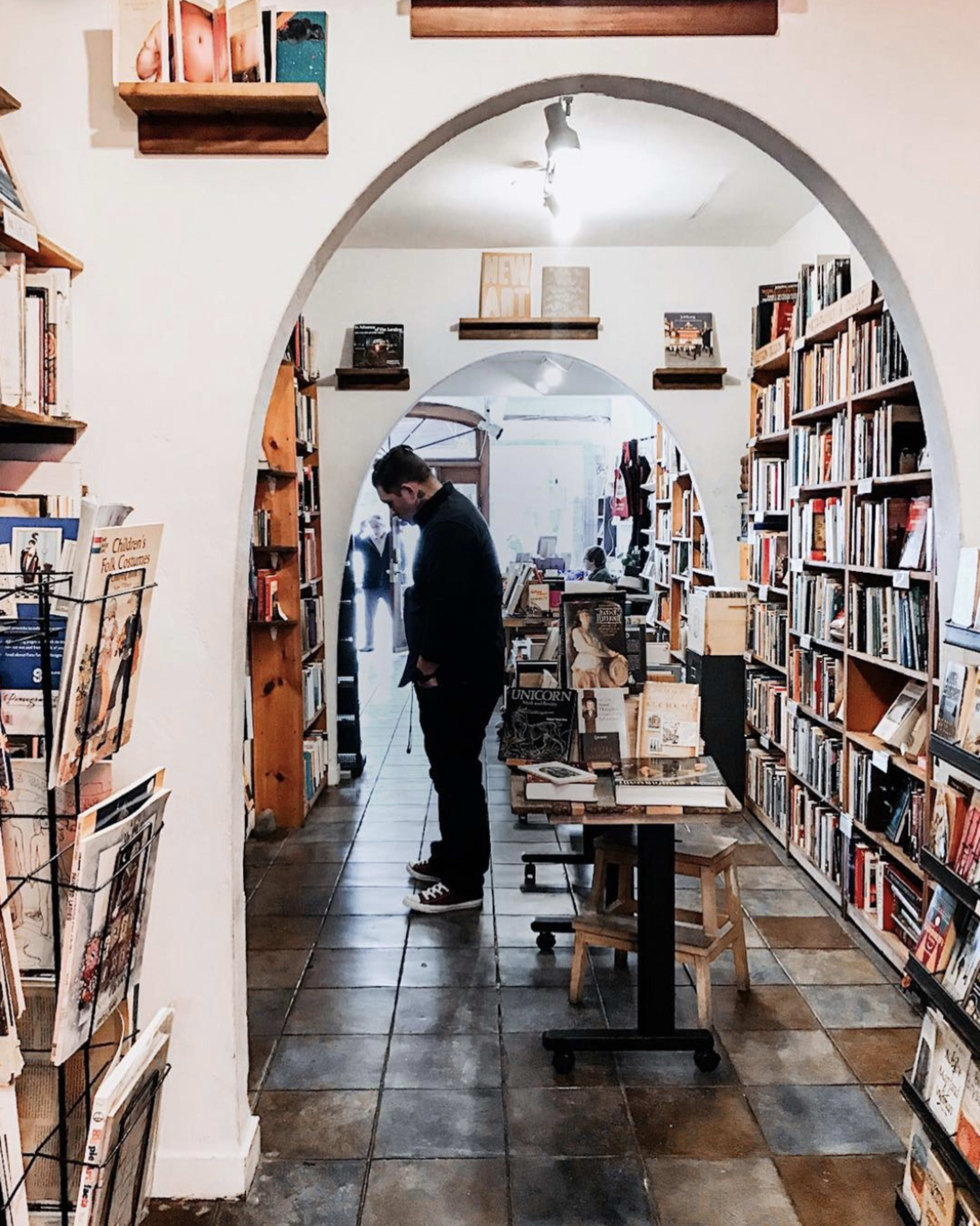 A person stands in a narrow aisle of a bookstore surrounded by shelves filled with books.