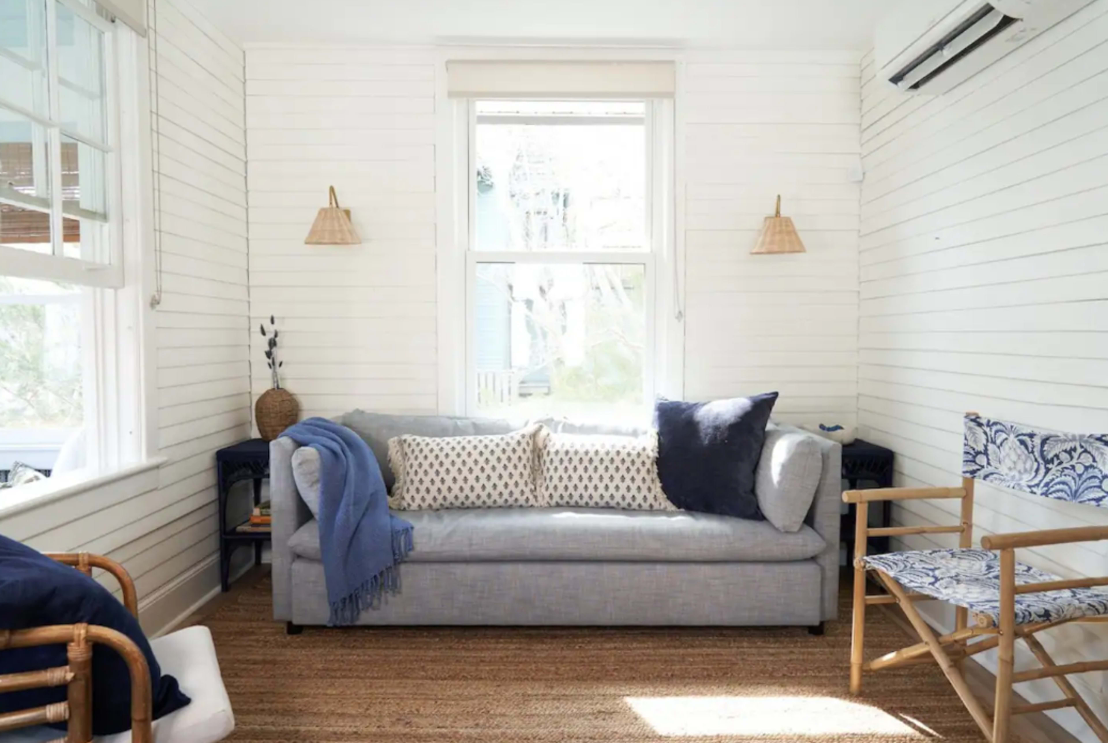 A light-filled living room with a gray sofa, patterned throw pillows, and simple wooden furniture.