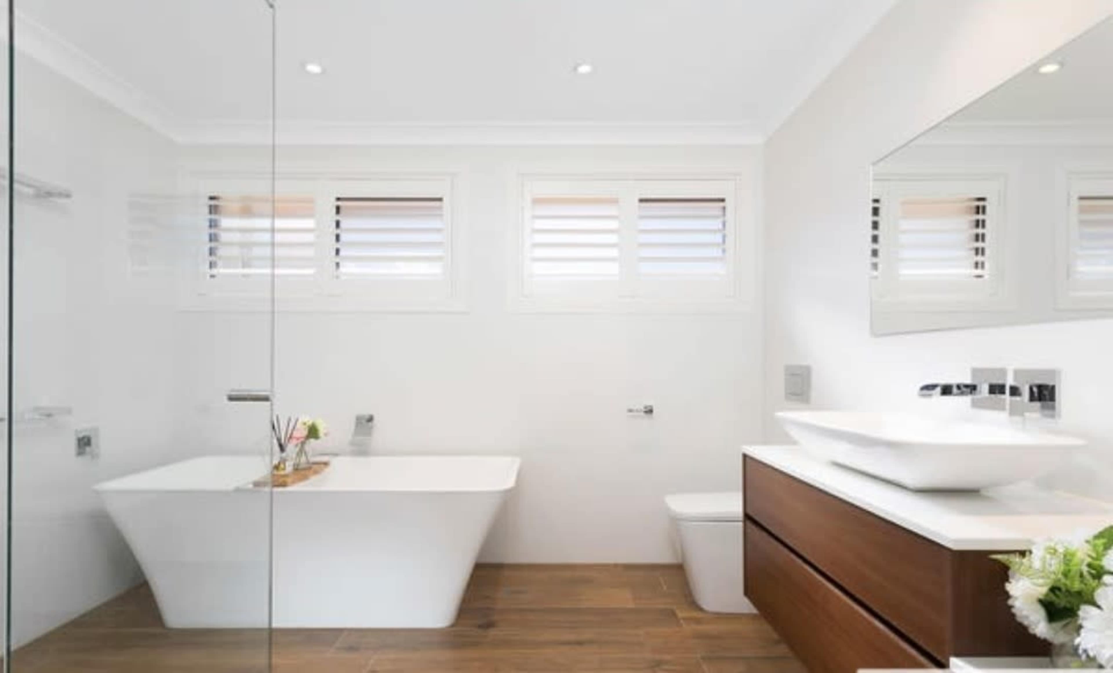 The image shows a modern bathroom featuring a freestanding bathtub, a wall-mounted sink, and a wooden vanity with a mirror.