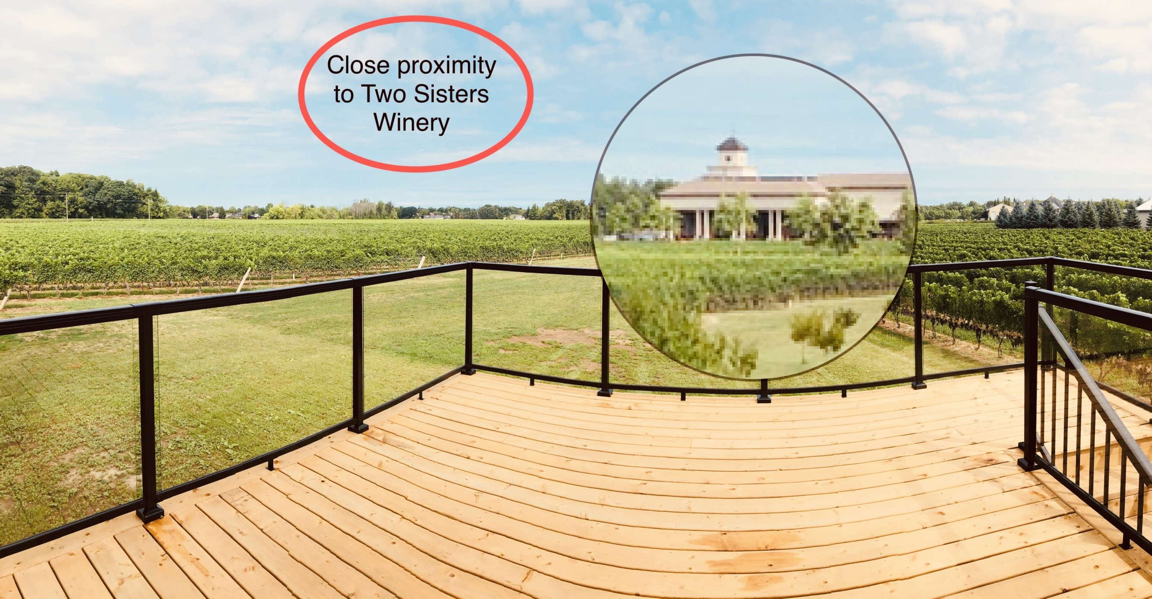 A wooden deck overlooking a vineyard with a building in the distance labeled as Two Sisters Winery.