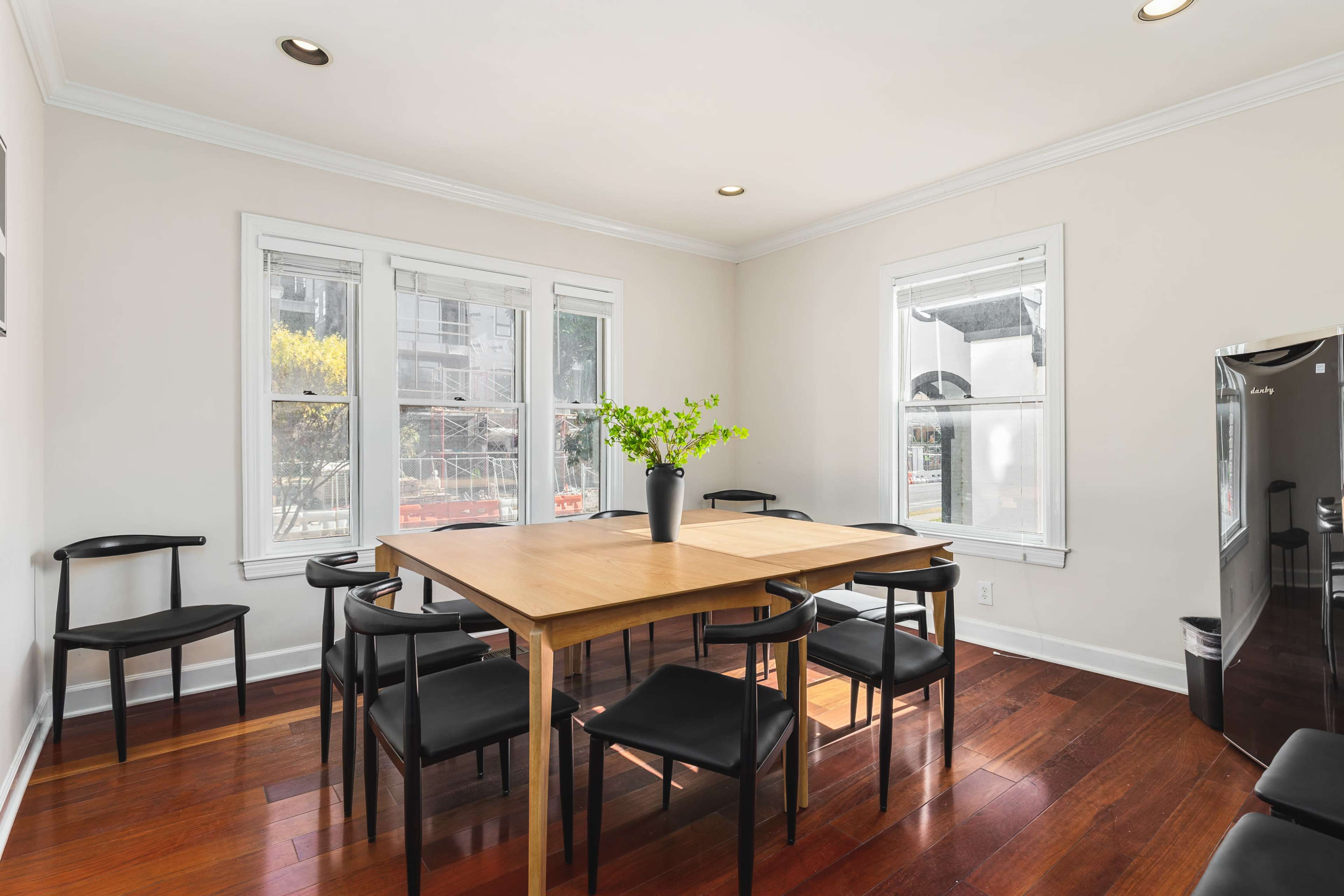 A dining area features a wooden table surrounded by black chairs and large windows allowing natural light.