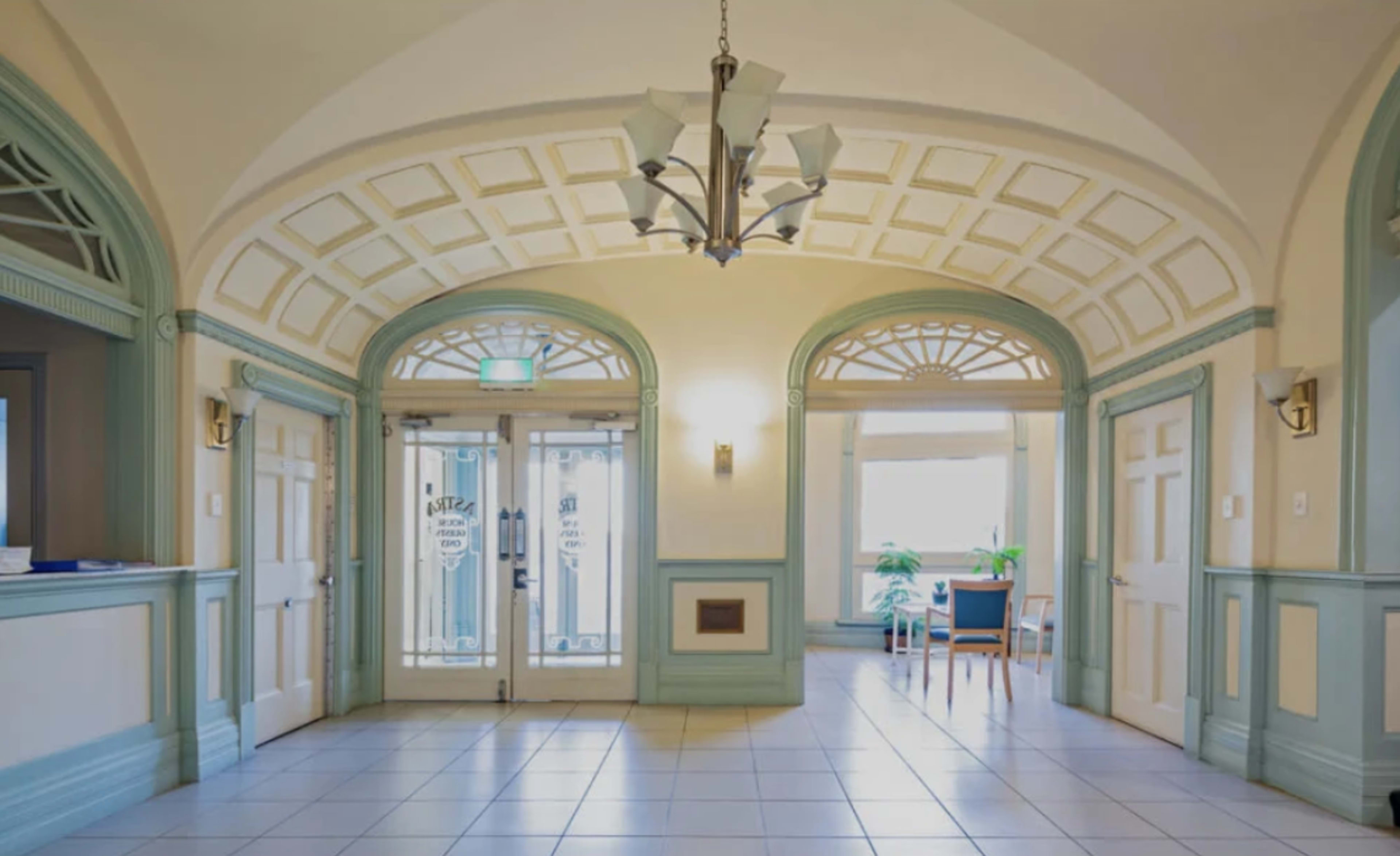 An elegant hallway with arched ceilings, two glass-paneled doors at the entrance, and a seating area beside a window.