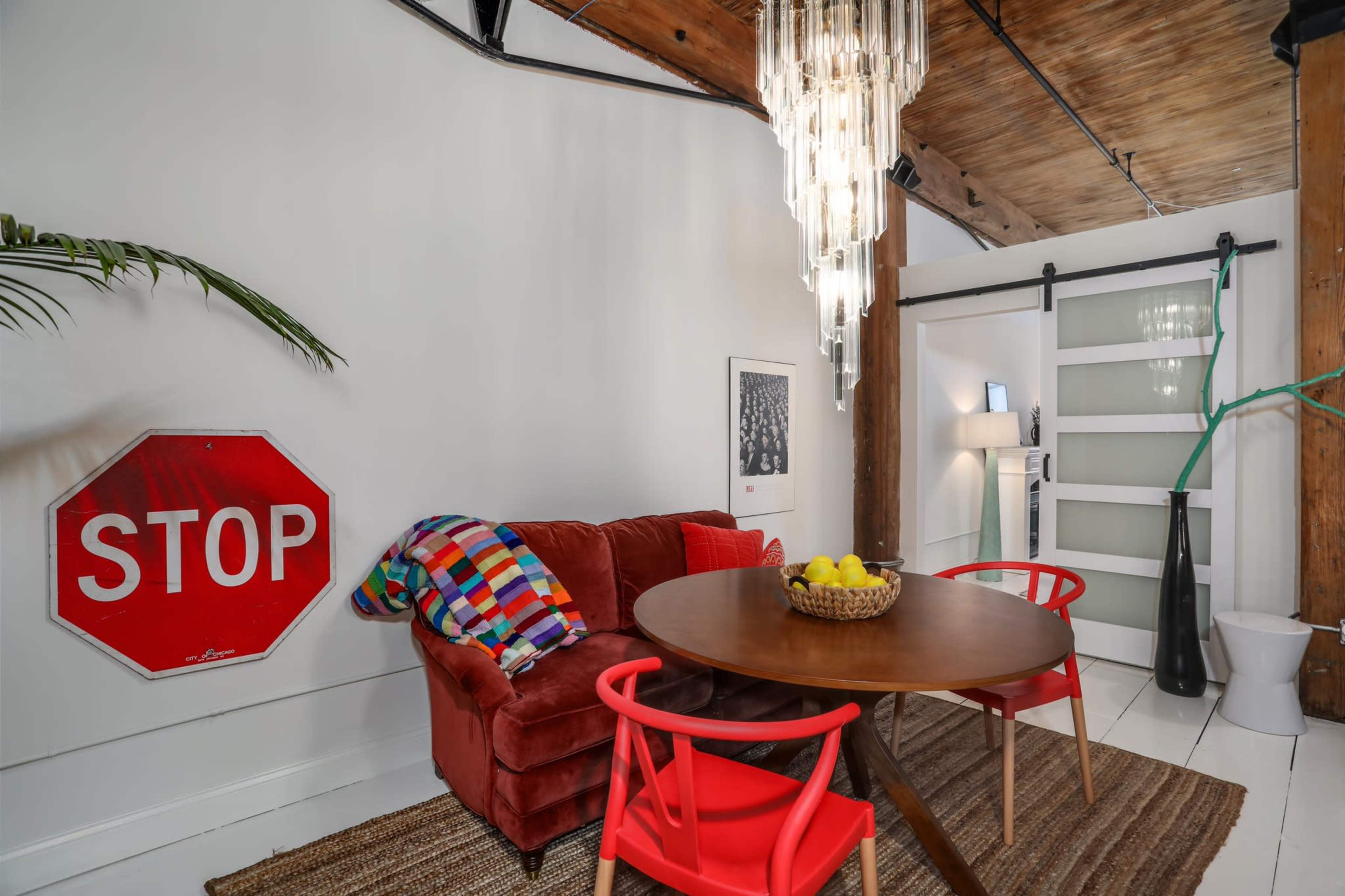 A cozy dining area featuring a round wooden table surrounded by red chairs, a plush red couch, and a large stop sign mounted on the wall.